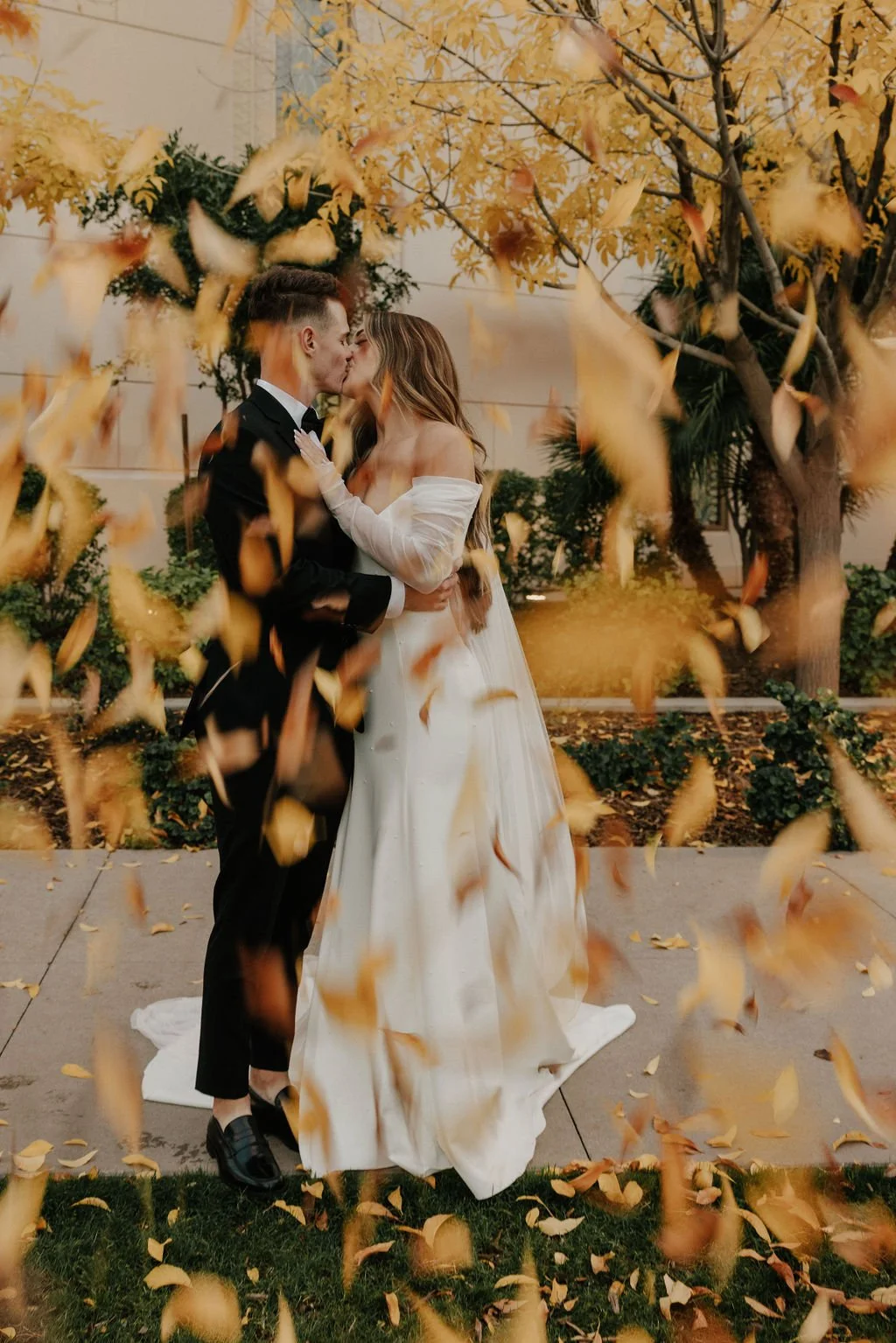 A couple holding hands in a desert landscape with large cacti and dry bushes during sunset, with the woman holding a bouquet of flowers.