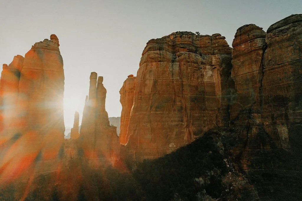 Sunset over tall, rugged red rock formations with rays of sunlight visible.