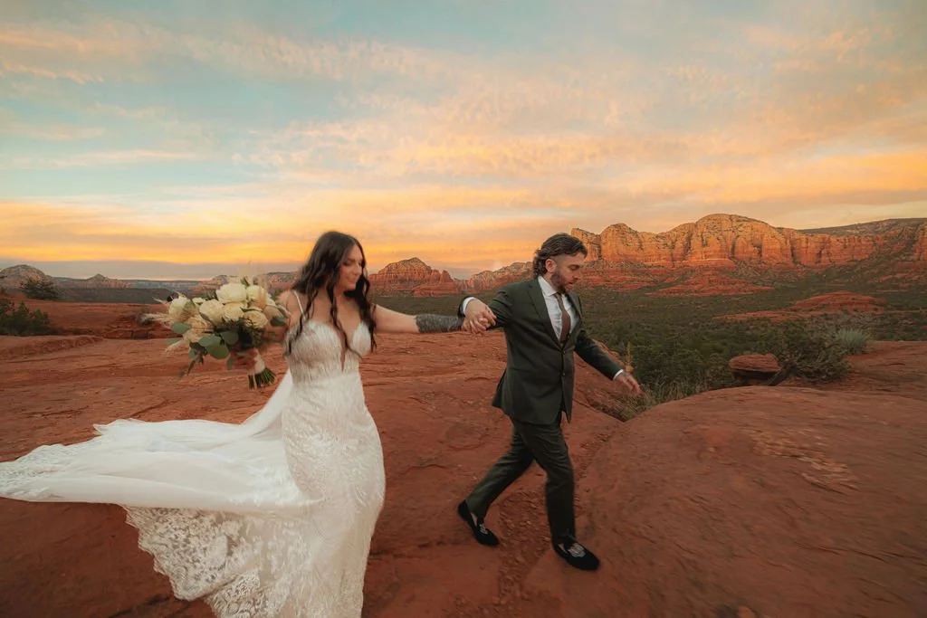 Bride and groom holding hands walking on a red rock landscape in Arizona during sunset