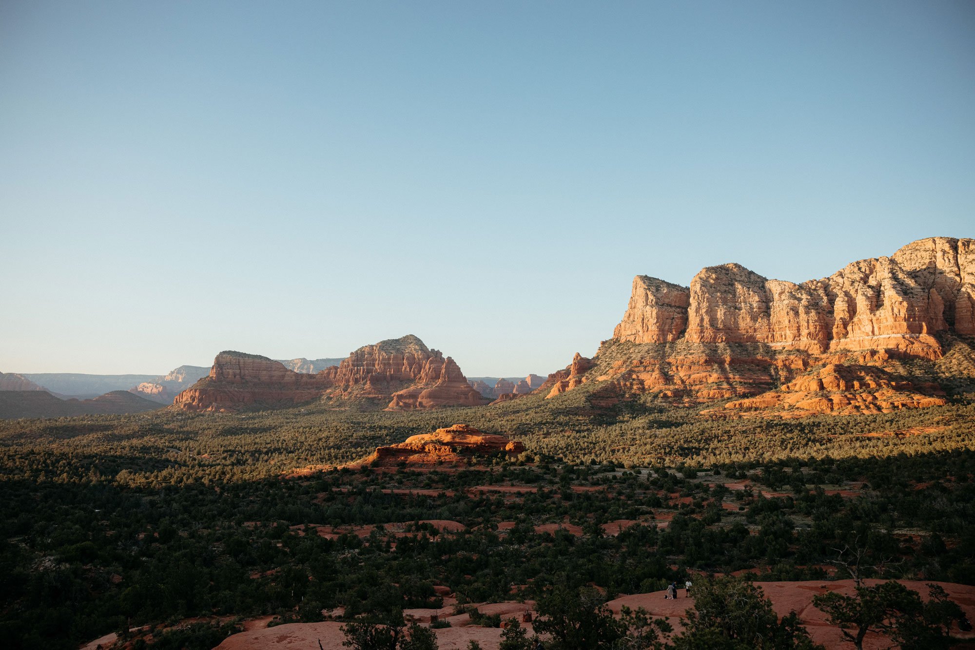 A scenic view of red rock formations and mountains in a desert landscape near sunset or sunrise.