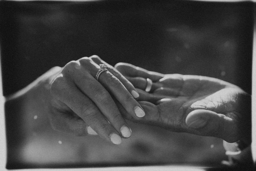 Hands gently touching, with rings on fingers, in black and white photo.
