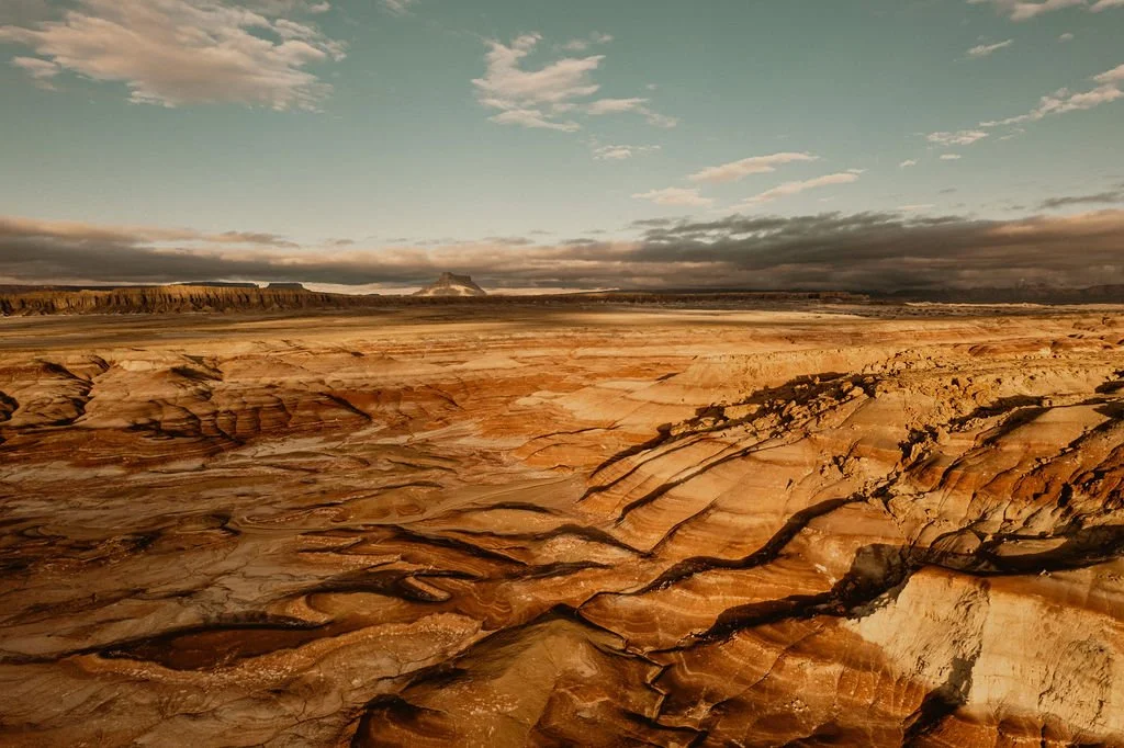 A vast desert landscape with layered rock formations and a cloudy sky overhead.
