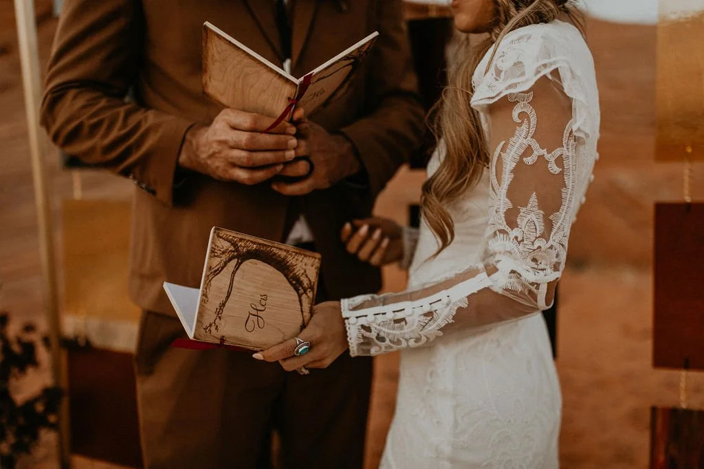A bride and groom holding a wedding prayer book during their ceremony, with the bride dressed in a white lace gown and the groom in a brown suit.