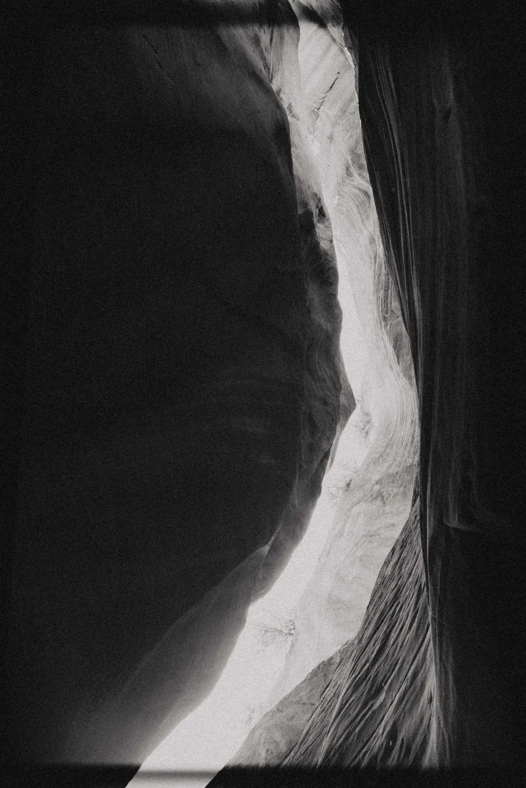 A black and white photograph of a narrow canyon with smooth, curved walls.