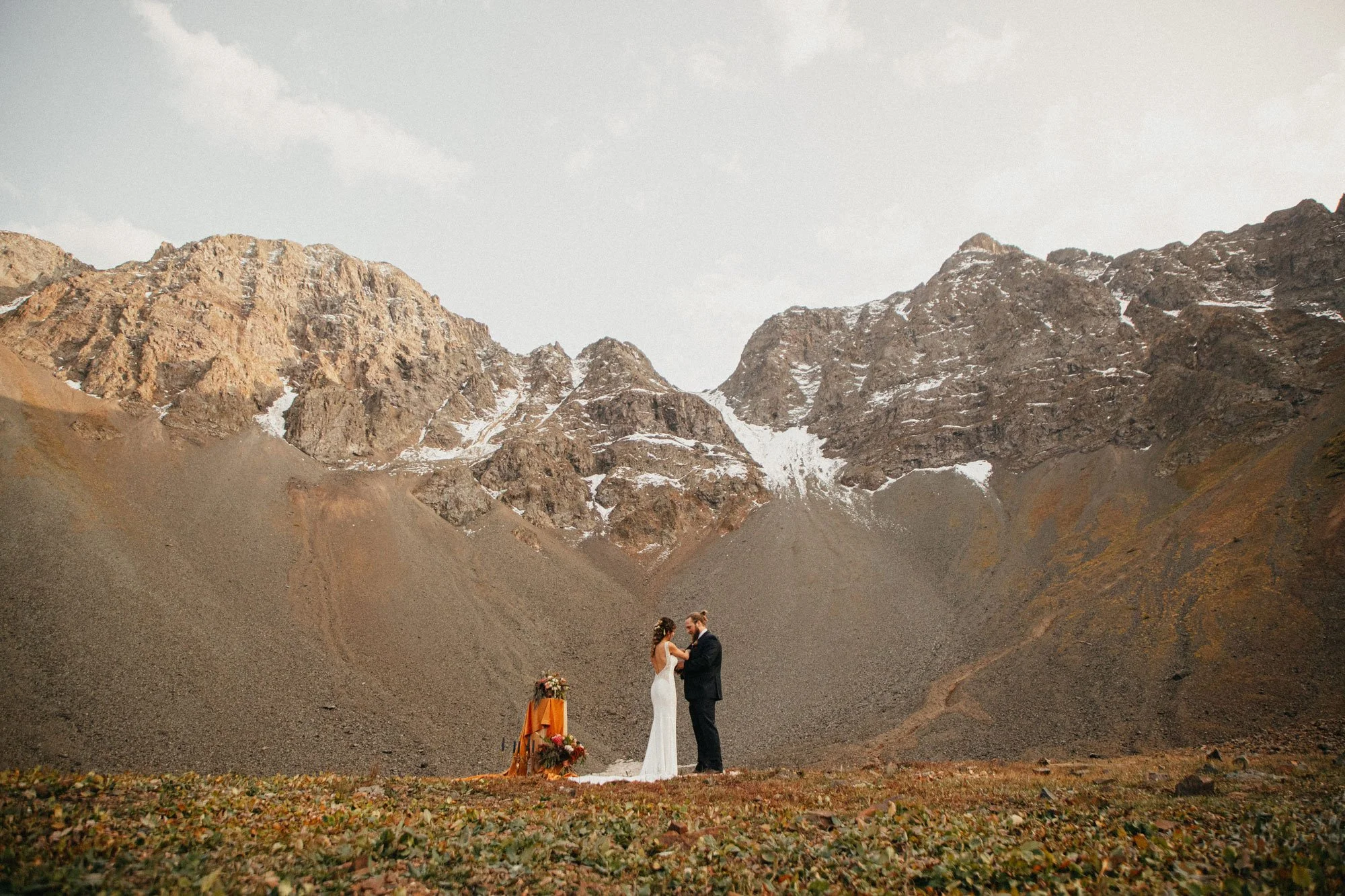 A bride and groom standing and holding hands in an outdoor wedding ceremony in Colorado, with a mountain range in the background.