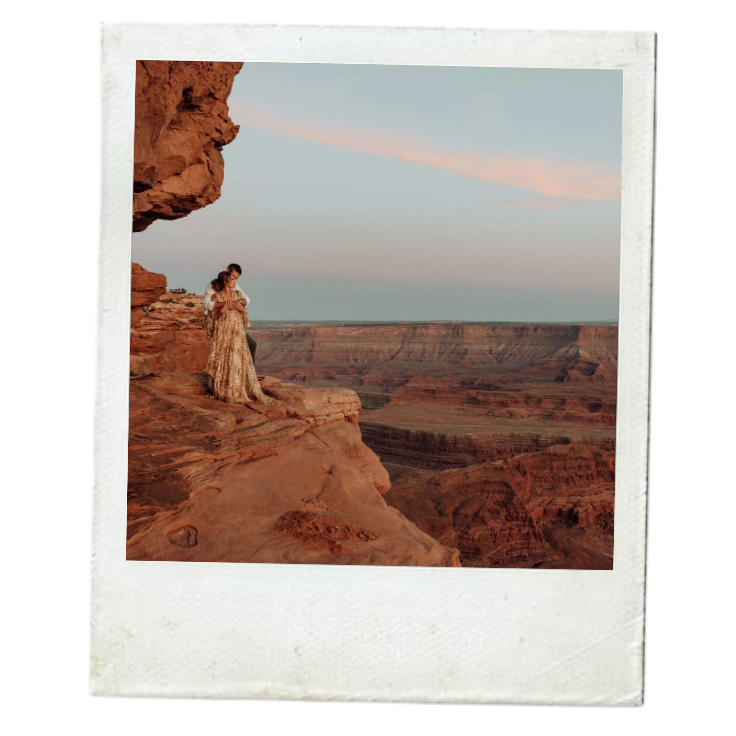 A person in a patterned dress standing on the edge of a rocky cliff at the Grand Canyon during sunset or sunrise.
