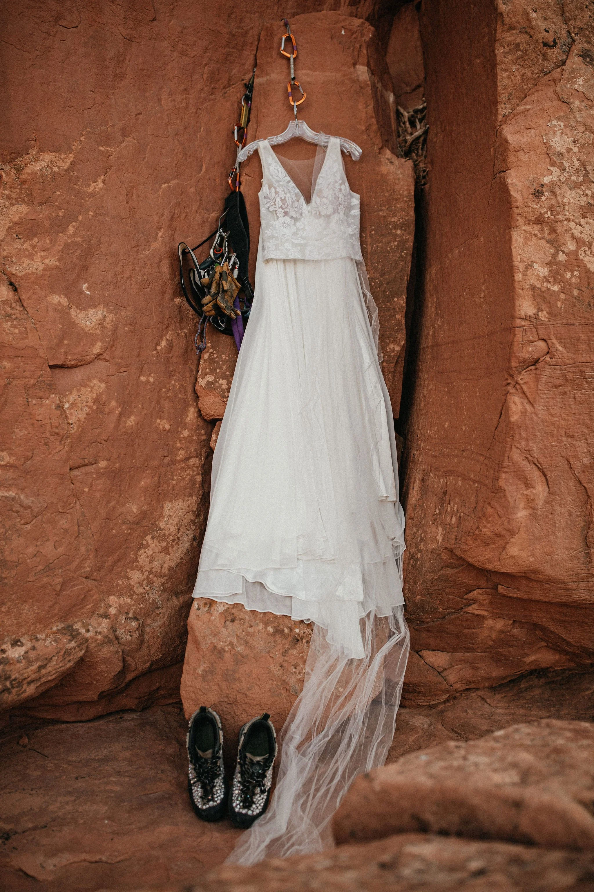 Wedding dress, shoes, and climbing gear hanging on a rock wall.