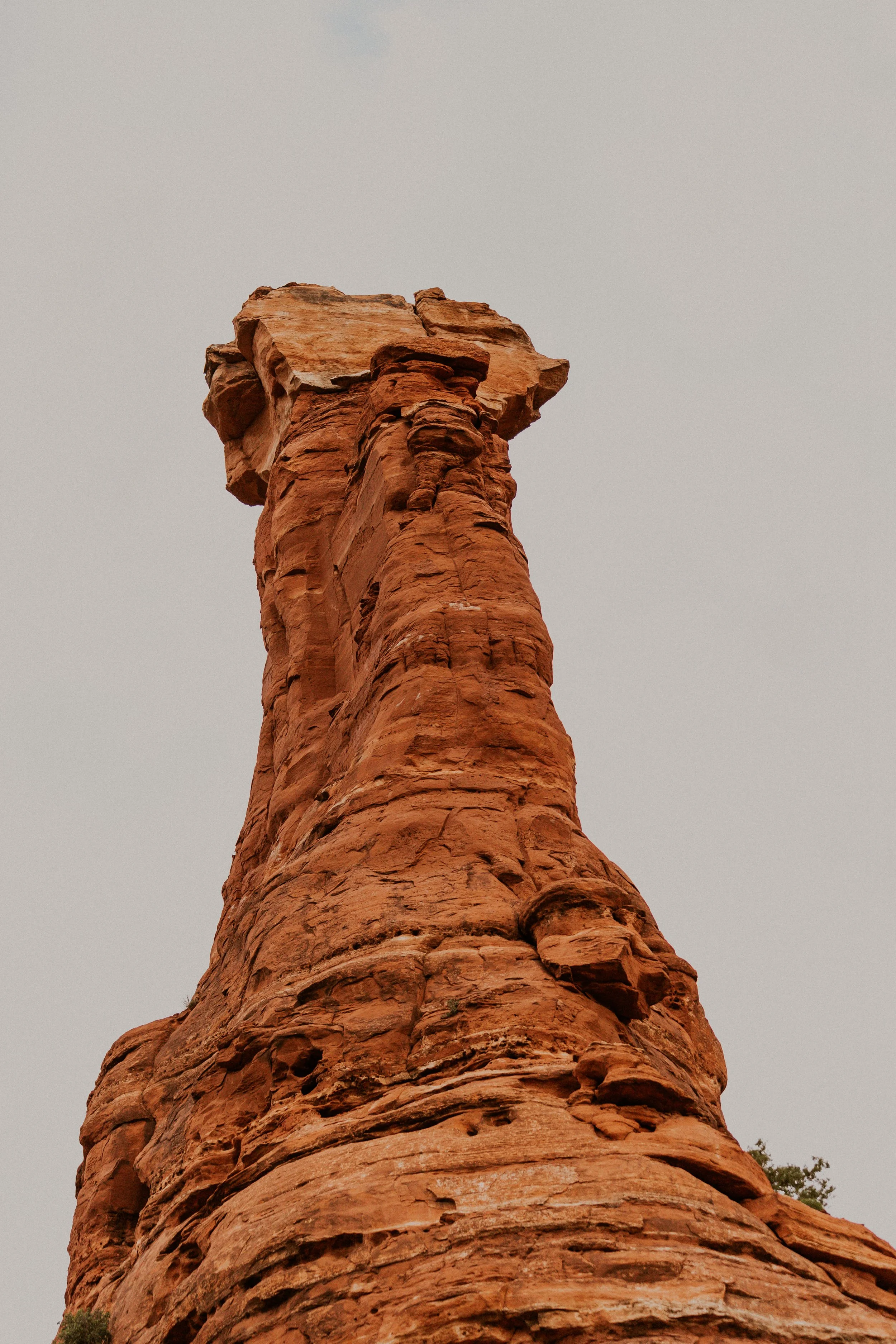 A tall, reddish-brown rock formation with a flat top against a cloudy sky.