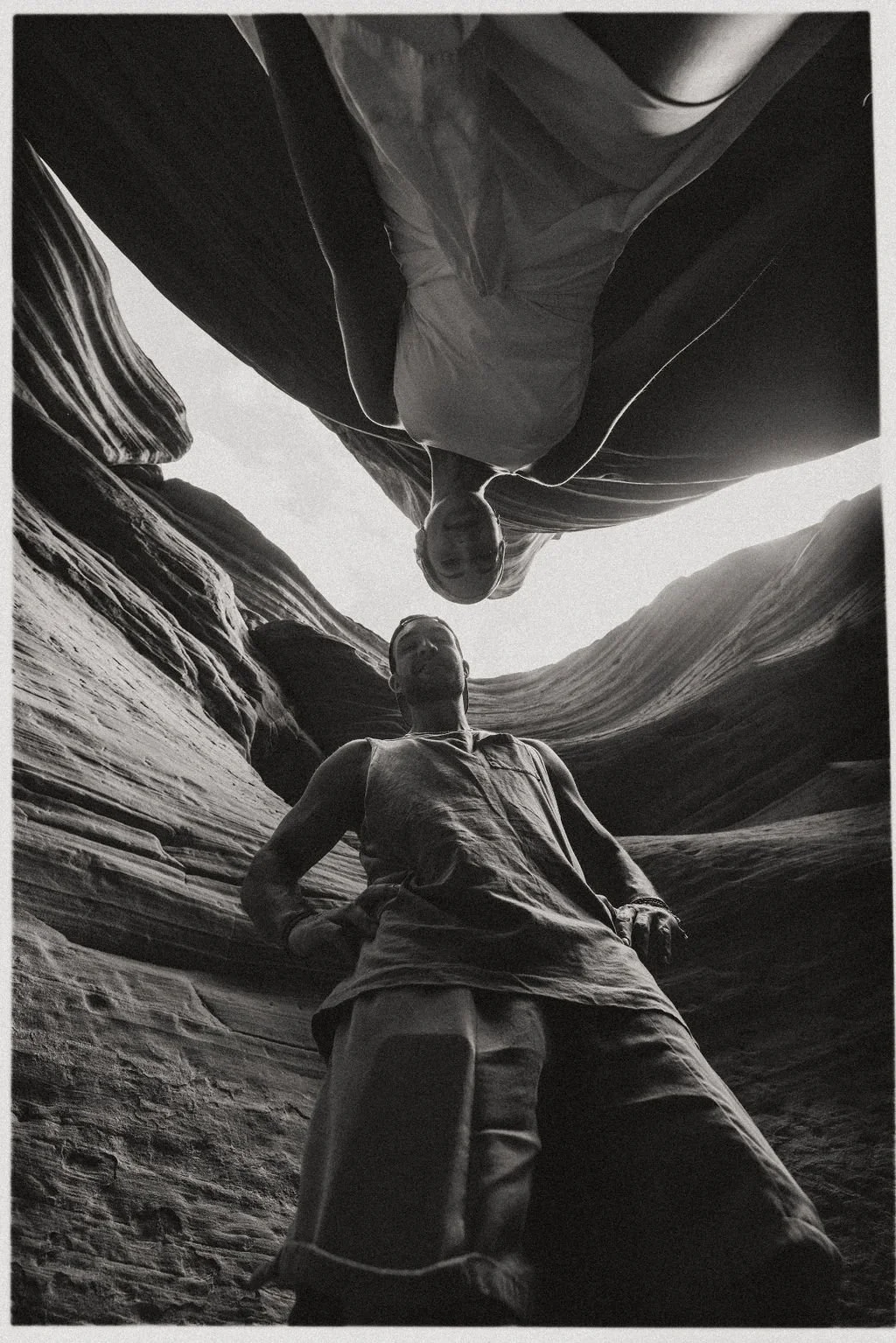 Two men standing inside a narrow, canyon-like rock formation, looking upward, with a view of the sky above.
