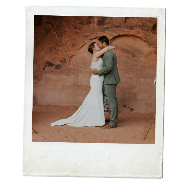 A bride and groom sharing a kiss in front of a reddish rock formation during their wedding or engagement photo shoot.