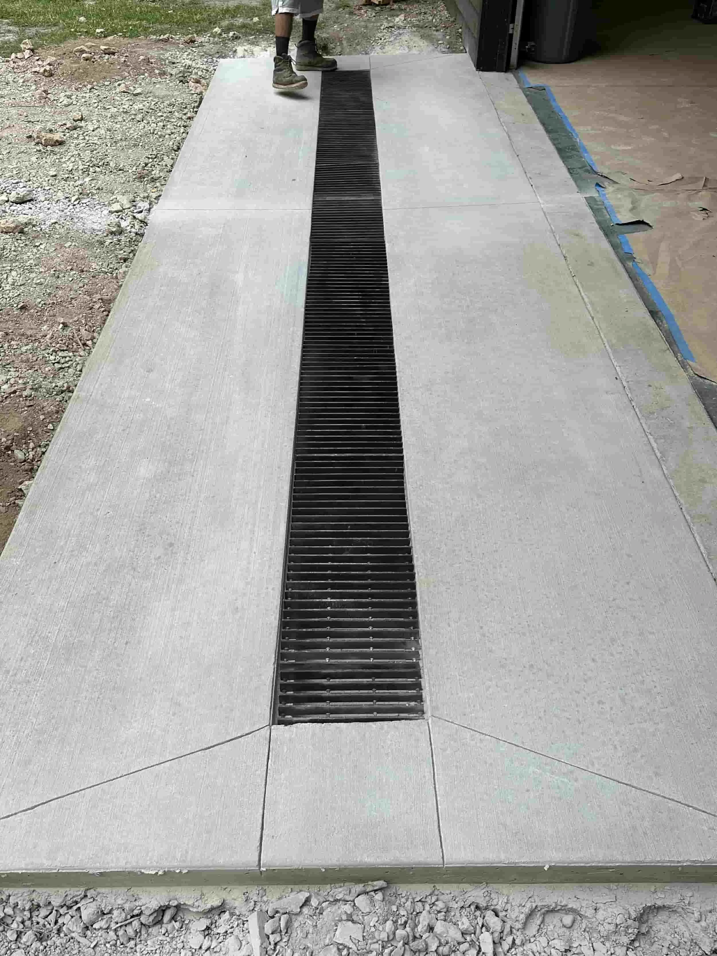 Concrete sidewalk with a centrally installed drainage grate and a person standing at the edge.