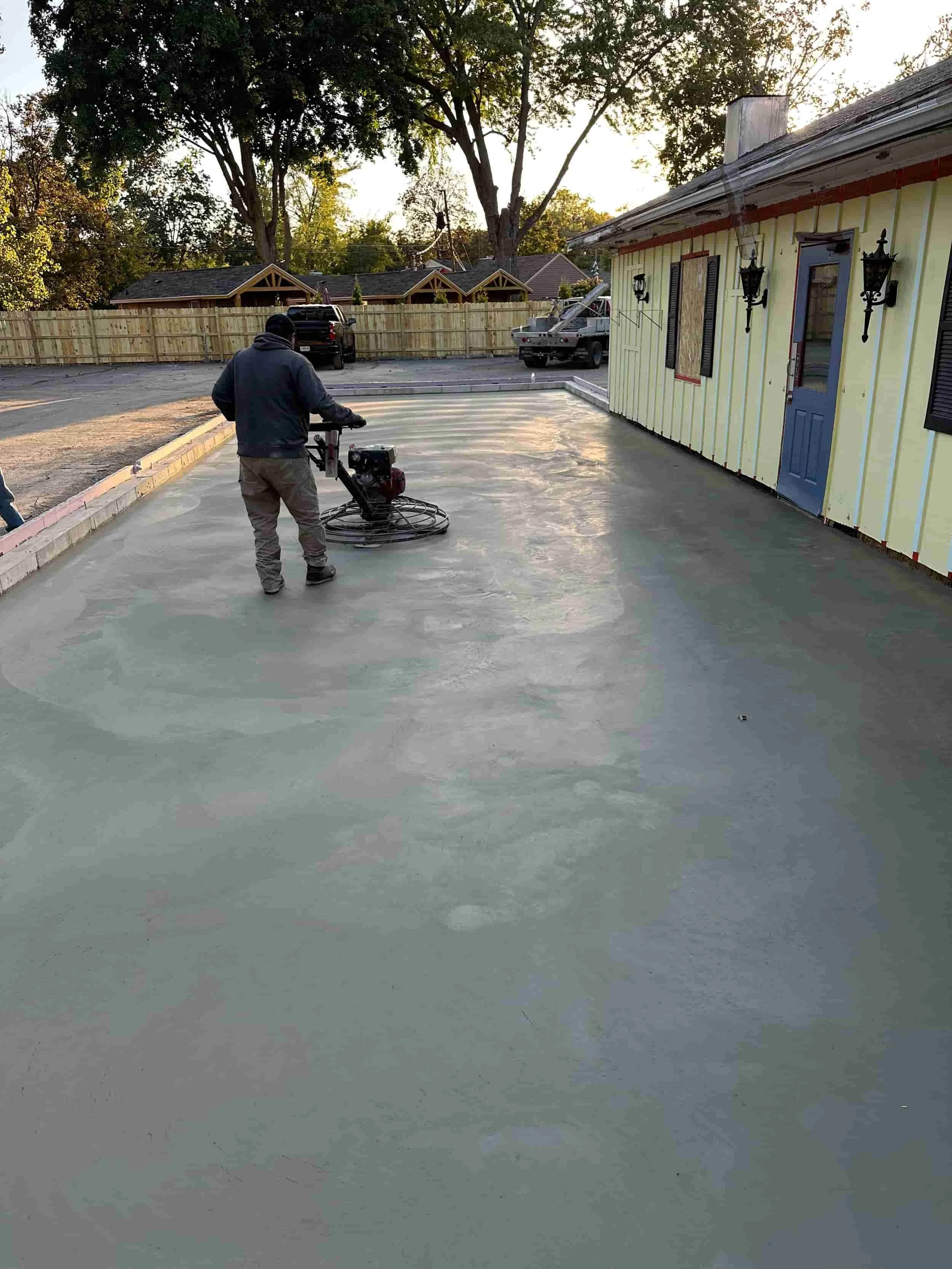 A person operating a concrete finishing machine on freshly poured concrete in a backyard.