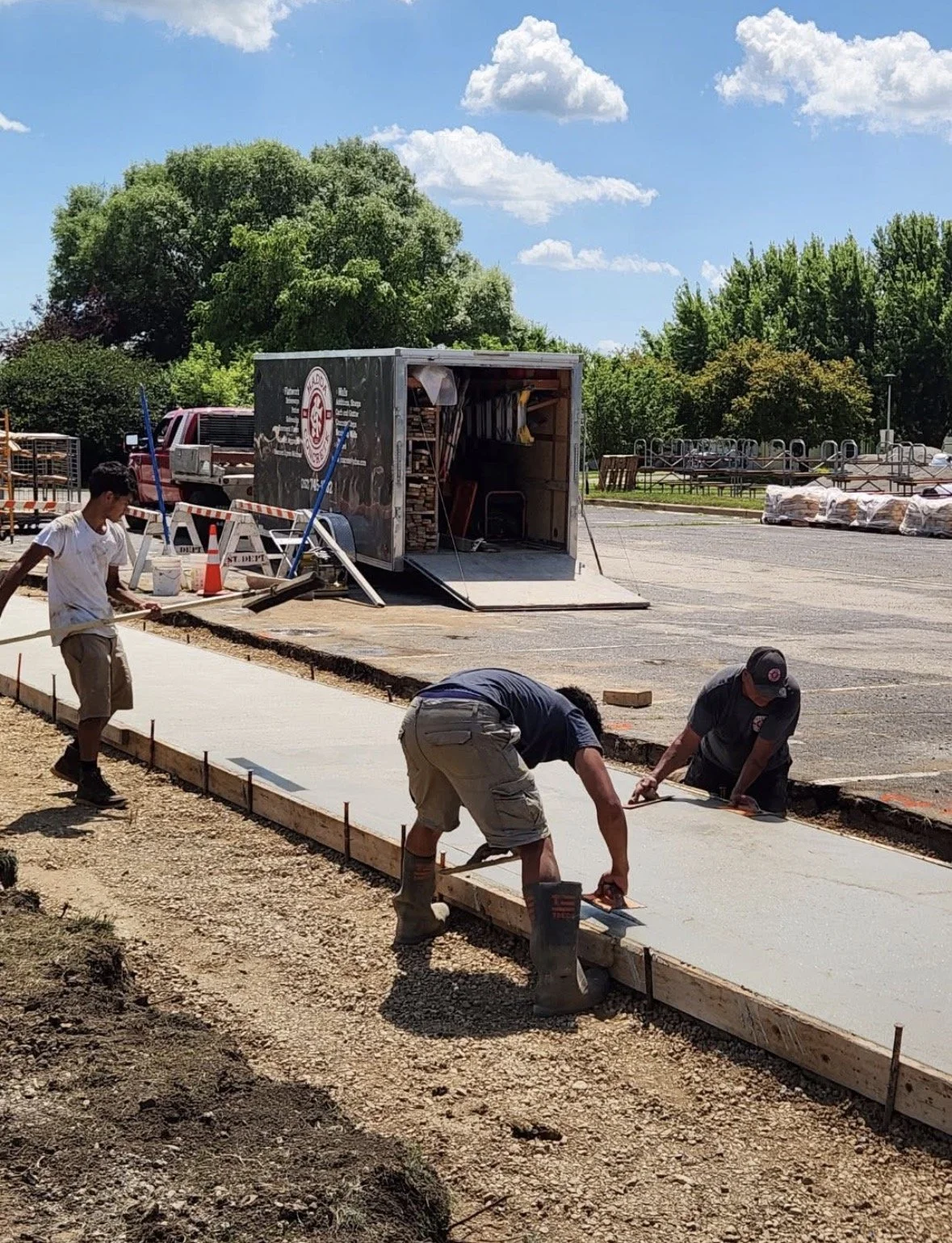 Construction workers pouring and leveling concrete on a sidewalk on a sunny day.
