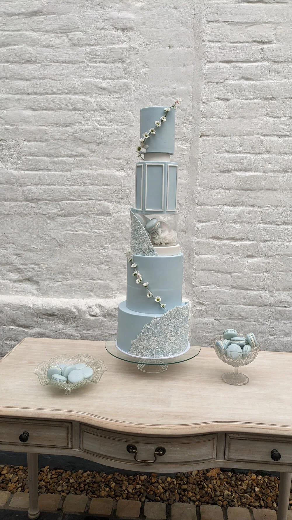 A tall, multi-tiered wedding cake decorated in light blue and white with floral accents and delicate lace-like patterns