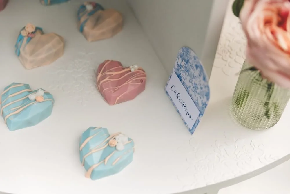 Heart-shaped biscuits decorated with pastel icing and pearls, arranged on a white display case