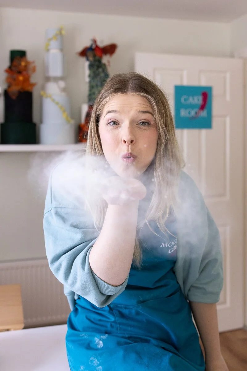Ruth blowing a cloud of flour toward the camera, dressed in a blue apron