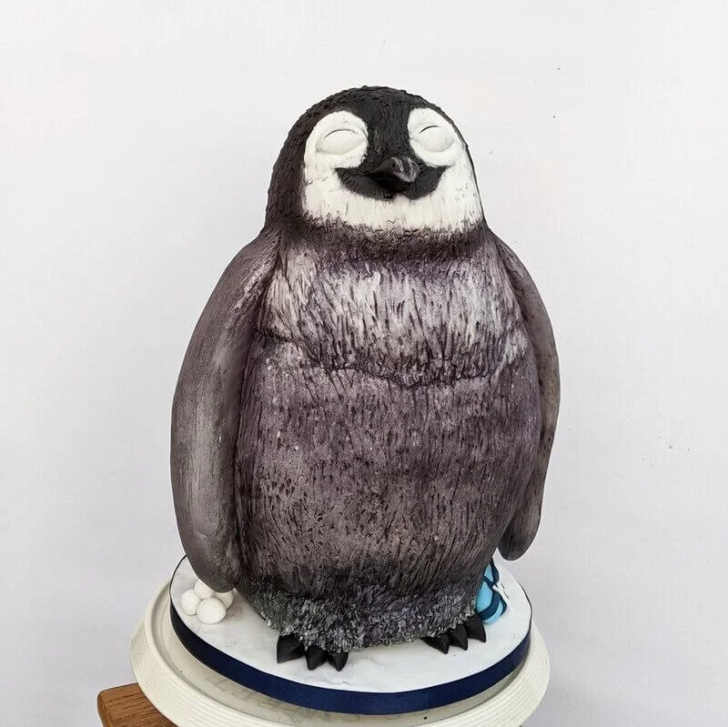 A carved birthday cake designed to look like a smiling penguin with closed eyes