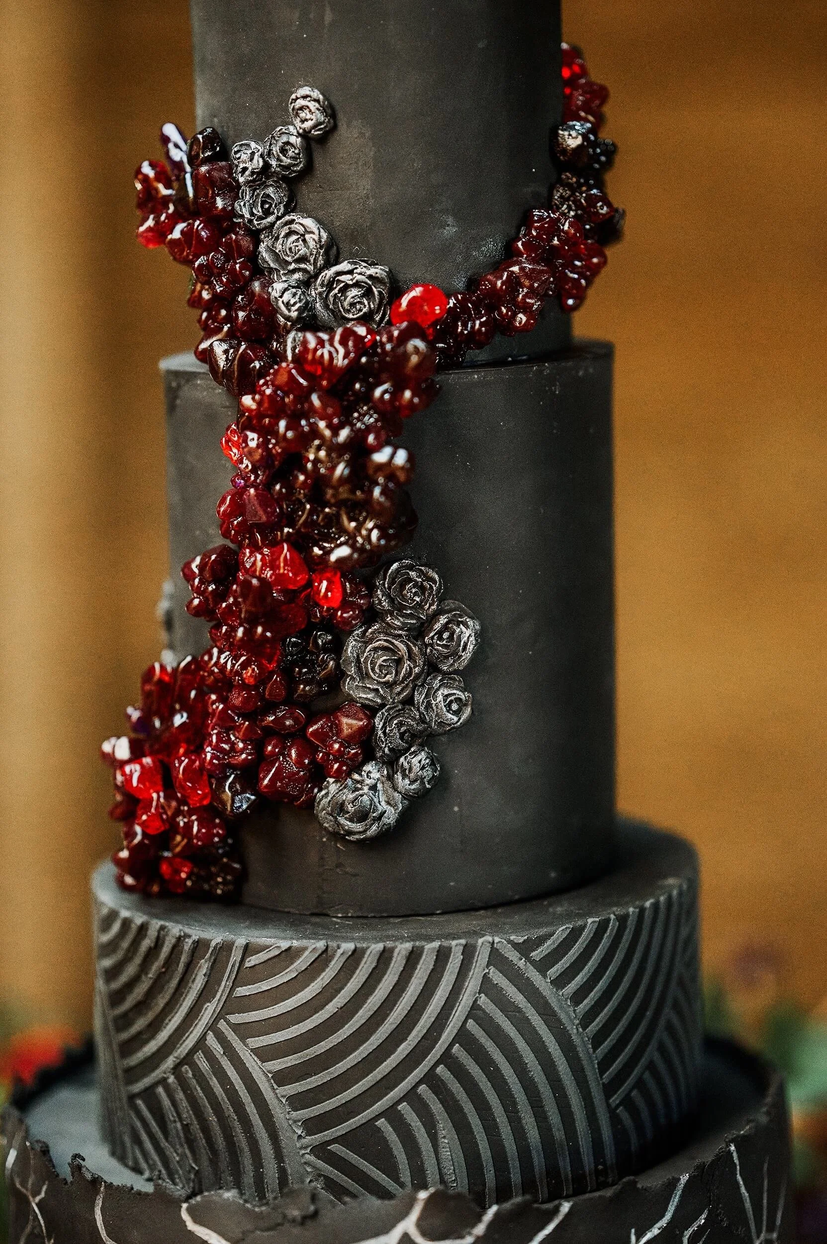 A black tiered cake decorated with silver roses and red berries.