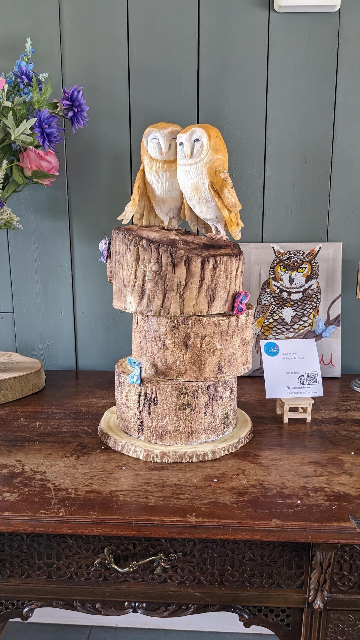 Carved cake of two owls perched on a tree stump display, with colourful butterfly decorations