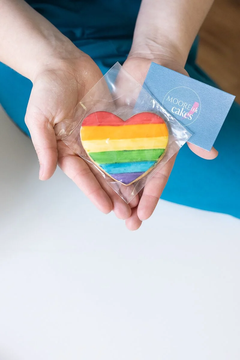Hands holding a rainbow iced heart-shaped cookie