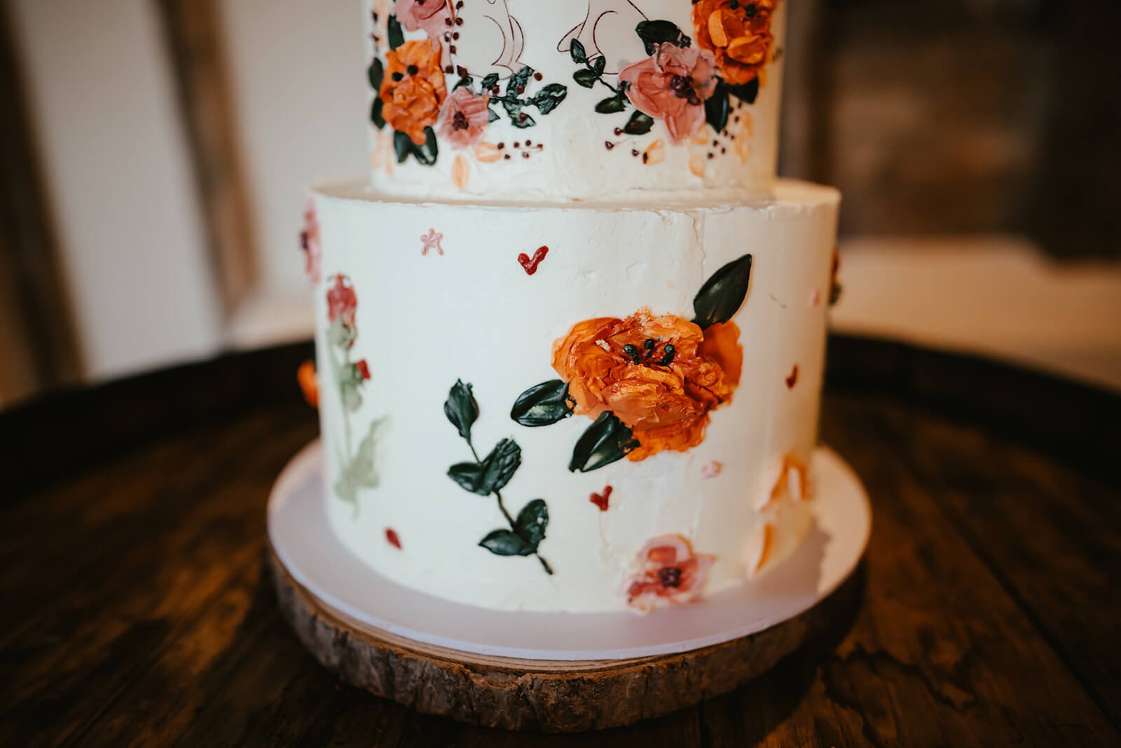 A two-tiered wedding cake with floral decorations and painted embellishments, placed on a table