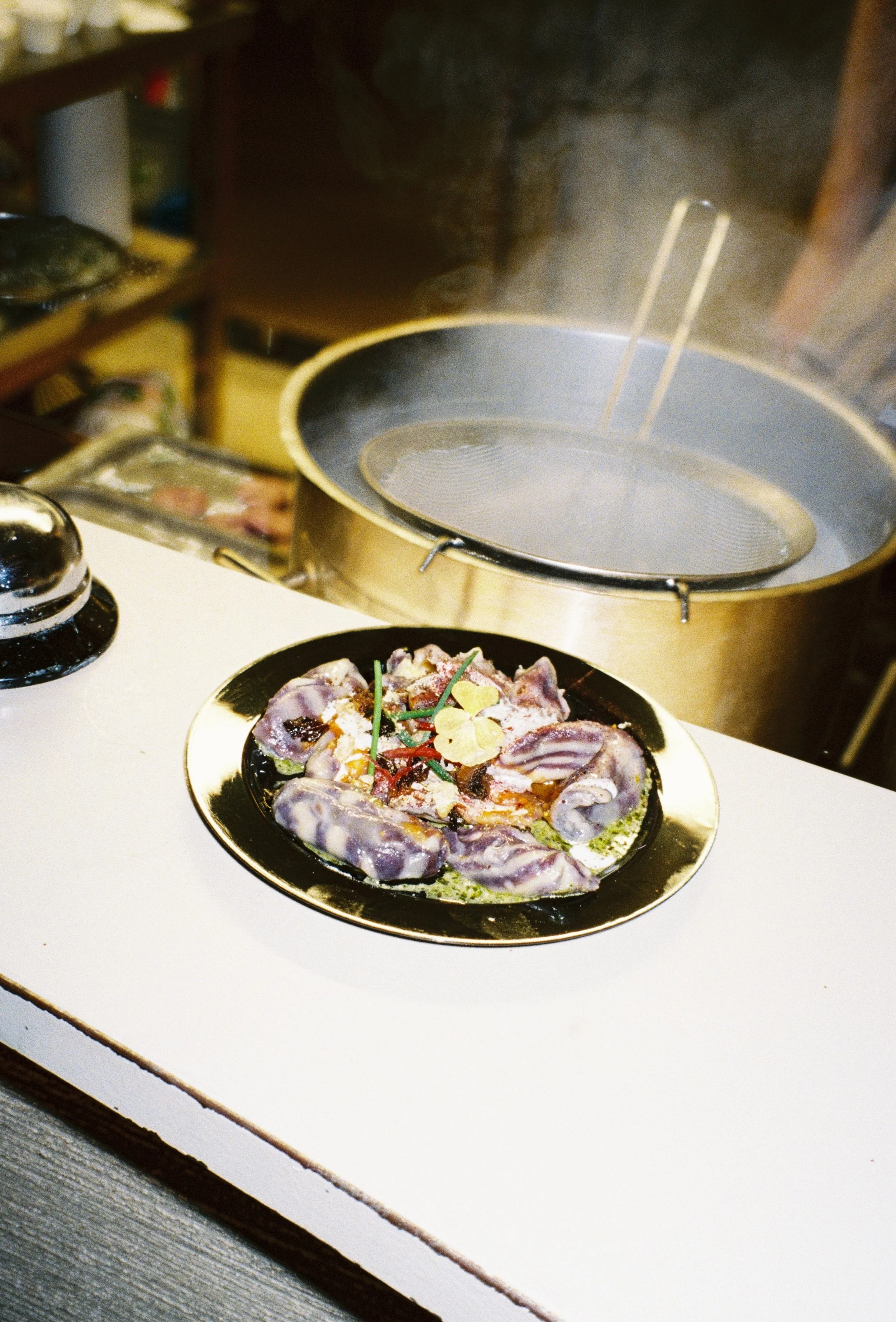 Plate of raw meat and herbs on a countertop, with a steaming hot pot in the background.