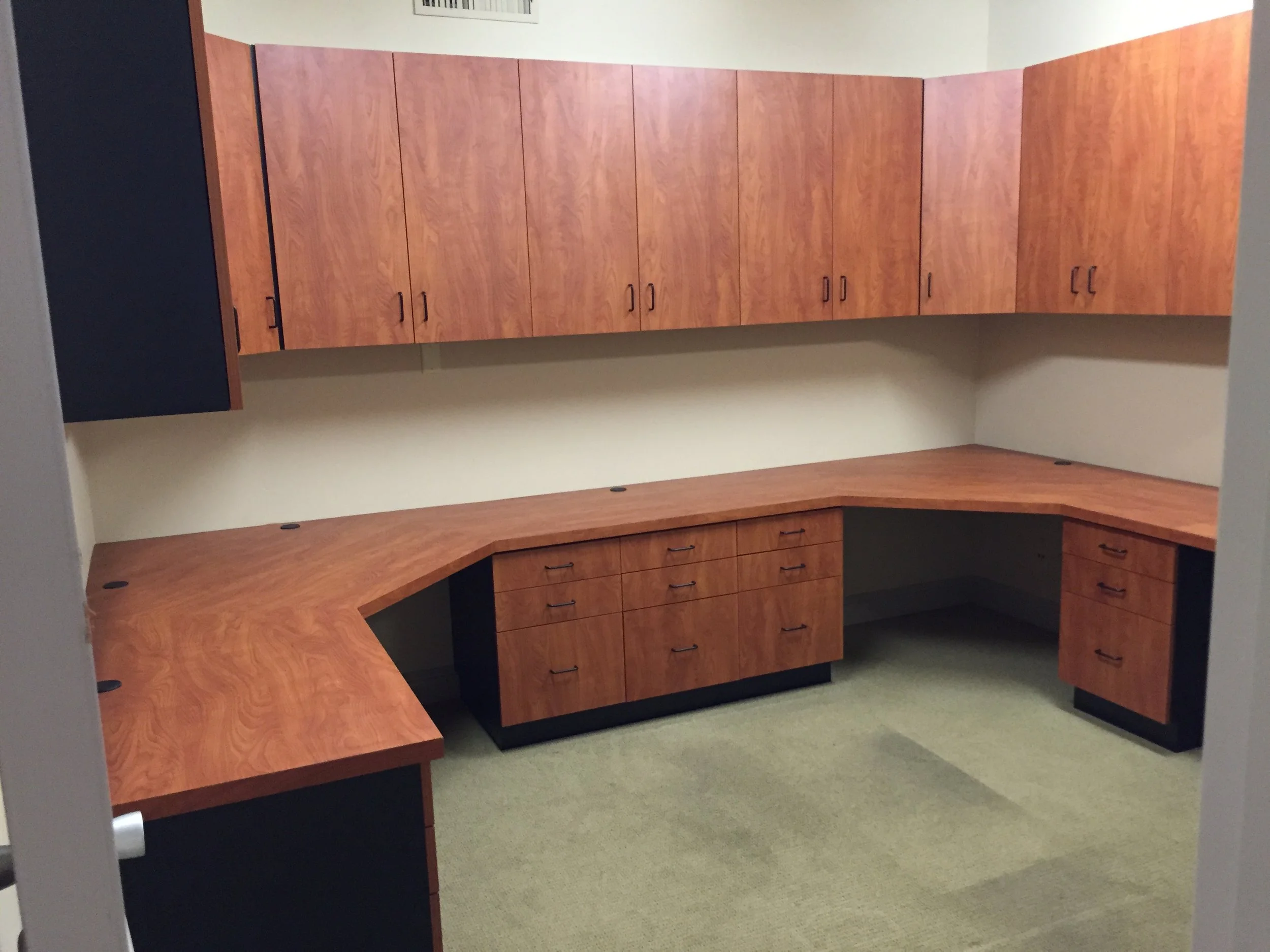 Empty office with wood laminate U-shaped desk and wall-mounted cabinets