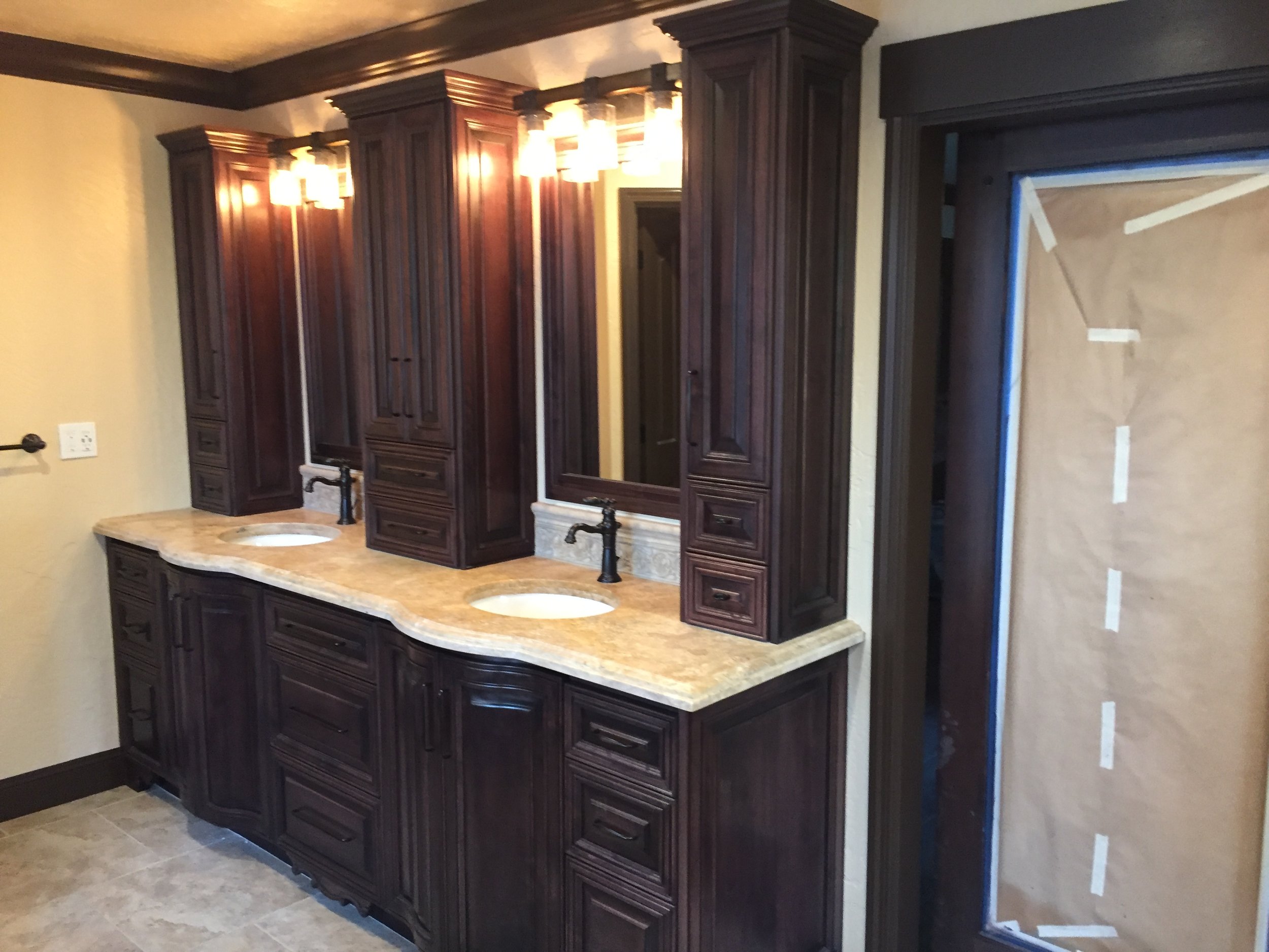 A double sink bathroom vanity with dark wooden cabinets, a beige marble countertop, two mirrors, and black fixtures. To the right, a doorway covered with brown paper and taped edges.