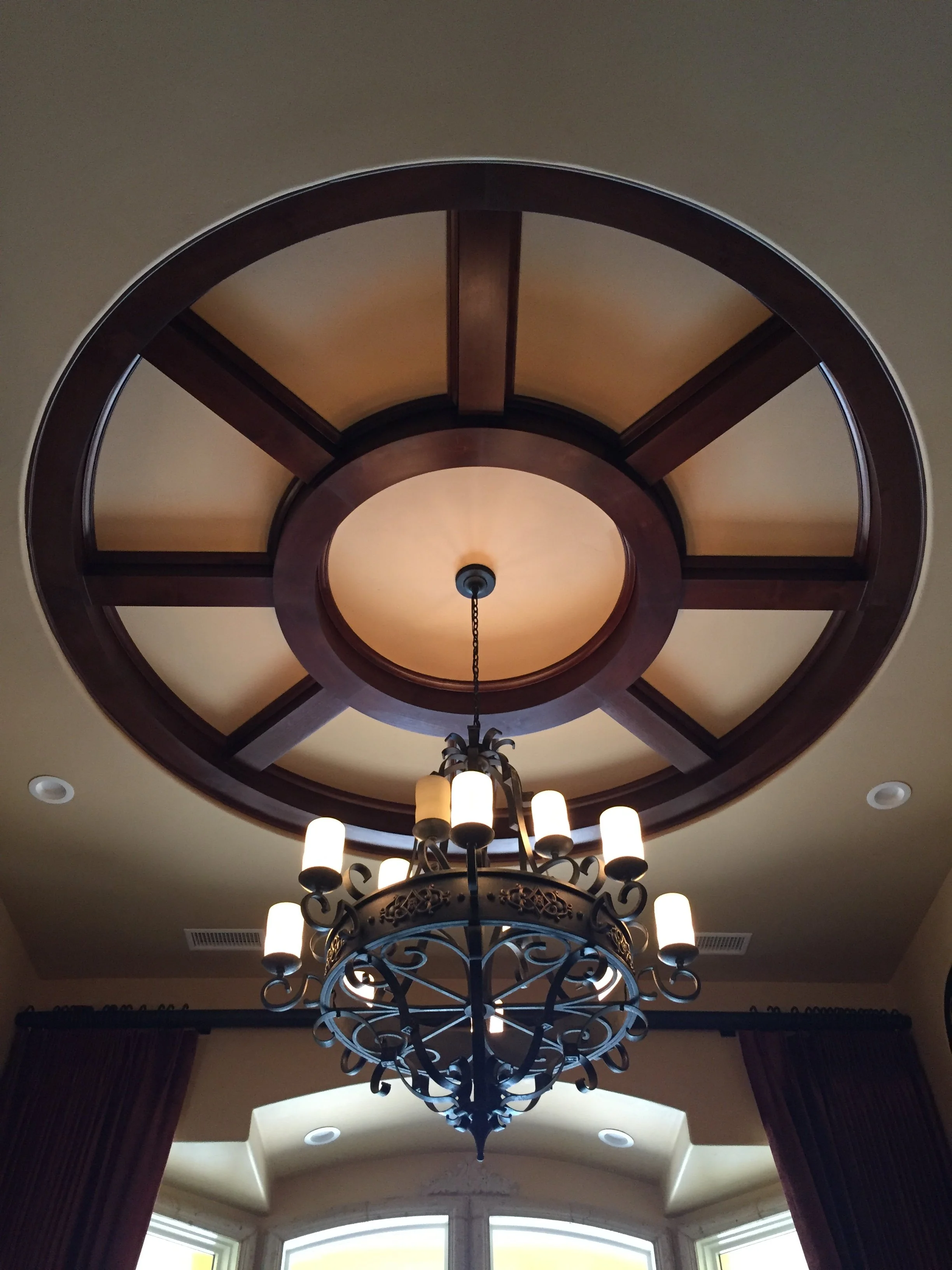View of a ceiling with a large circular wooden decorative feature and a chandelier hanging from the center.