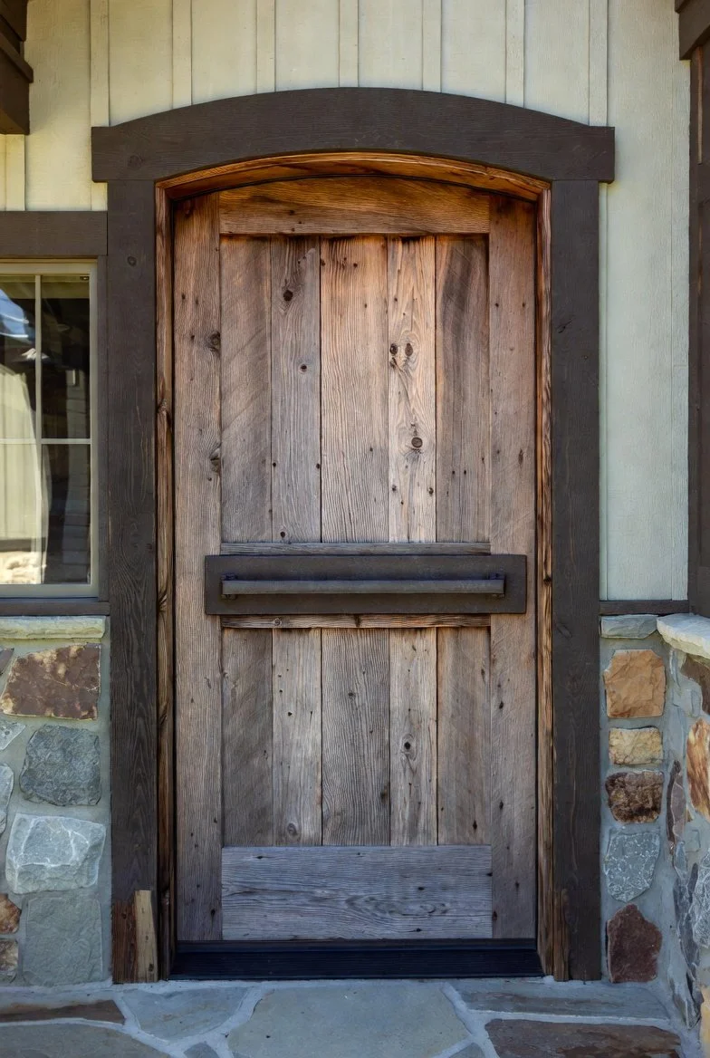 Wooden barn-style door with black trim/frame, set in a stone and stucco exterior wall.