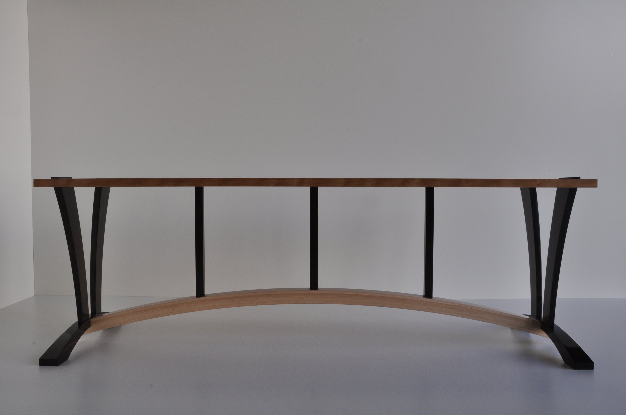 A modern, minimalist console table with a wooden top, black metal supports, and a curved wooden base.