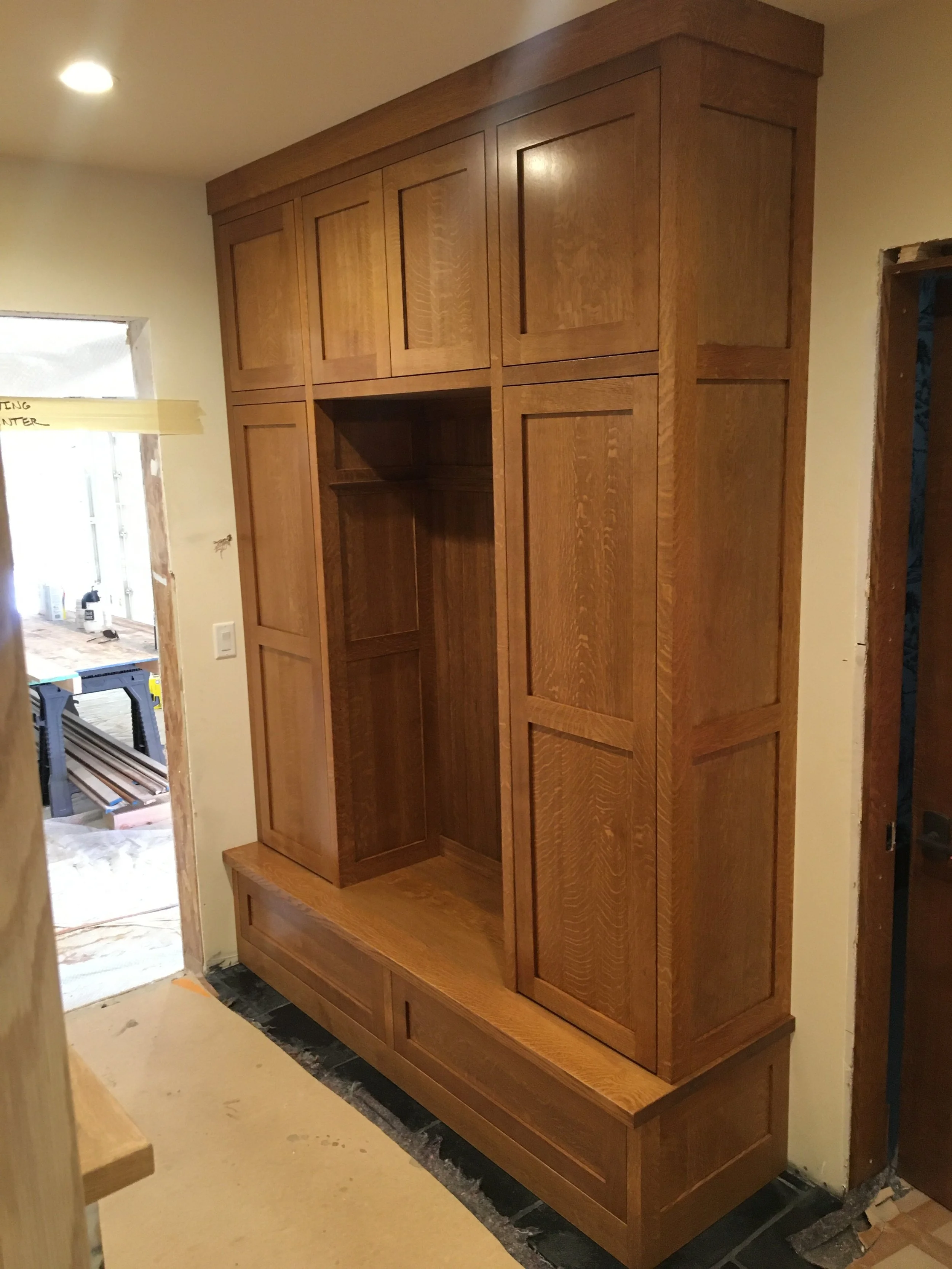 A large wooden built-in cabinet with multiple doors and drawers in a room under construction.