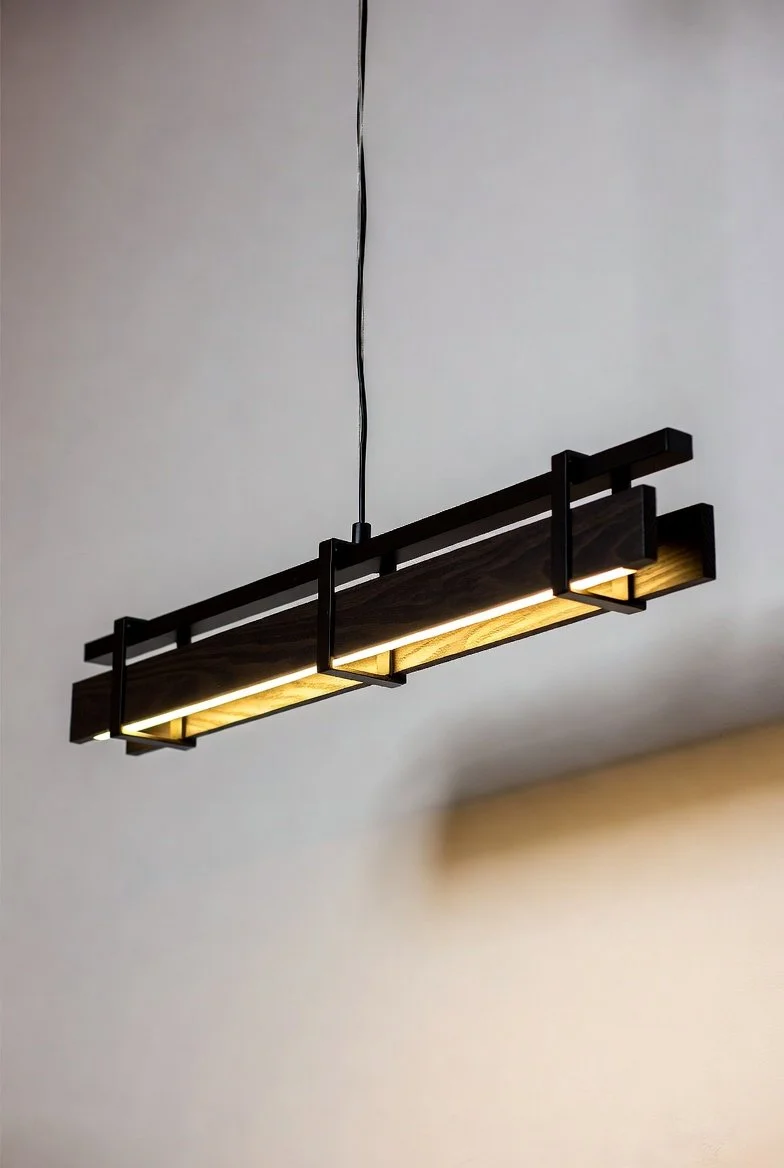 Modern black and wood rectangular pendant light fixture hanging from the ceiling above a light-colored wall.