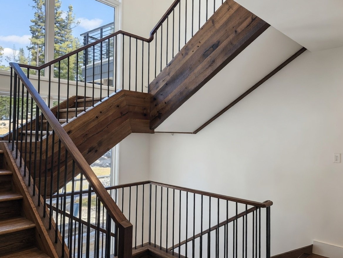 Empty staircase and landings inside a modern house, with large windows showing trees outside.