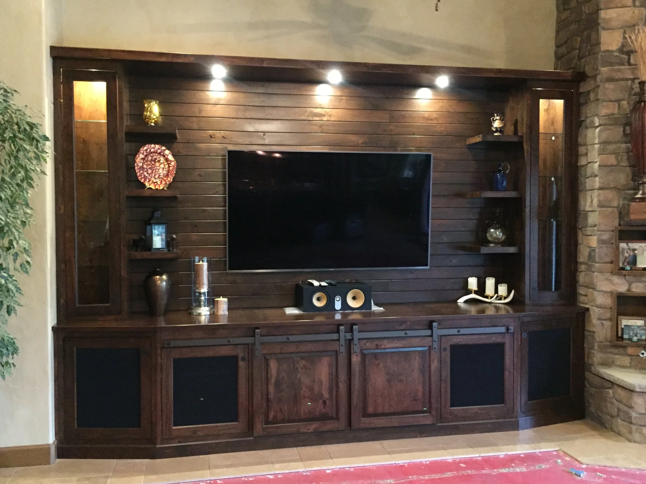 A dark wood entertainment center housing a flat screen TV, with decorative items on the shelves, against a wood-paneled wall with inset lighting.