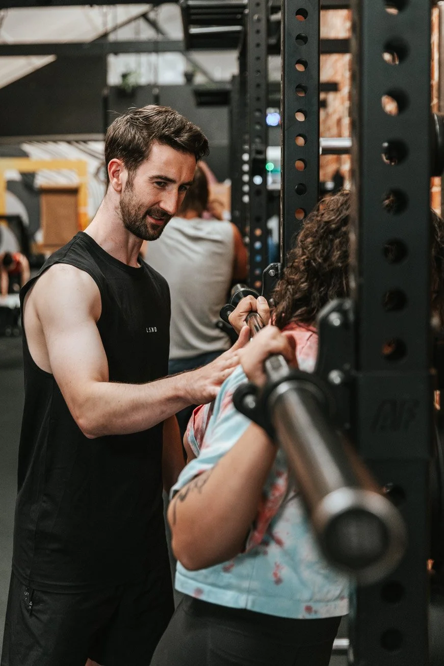 A man spotting a woman during weightlifting at a gym.