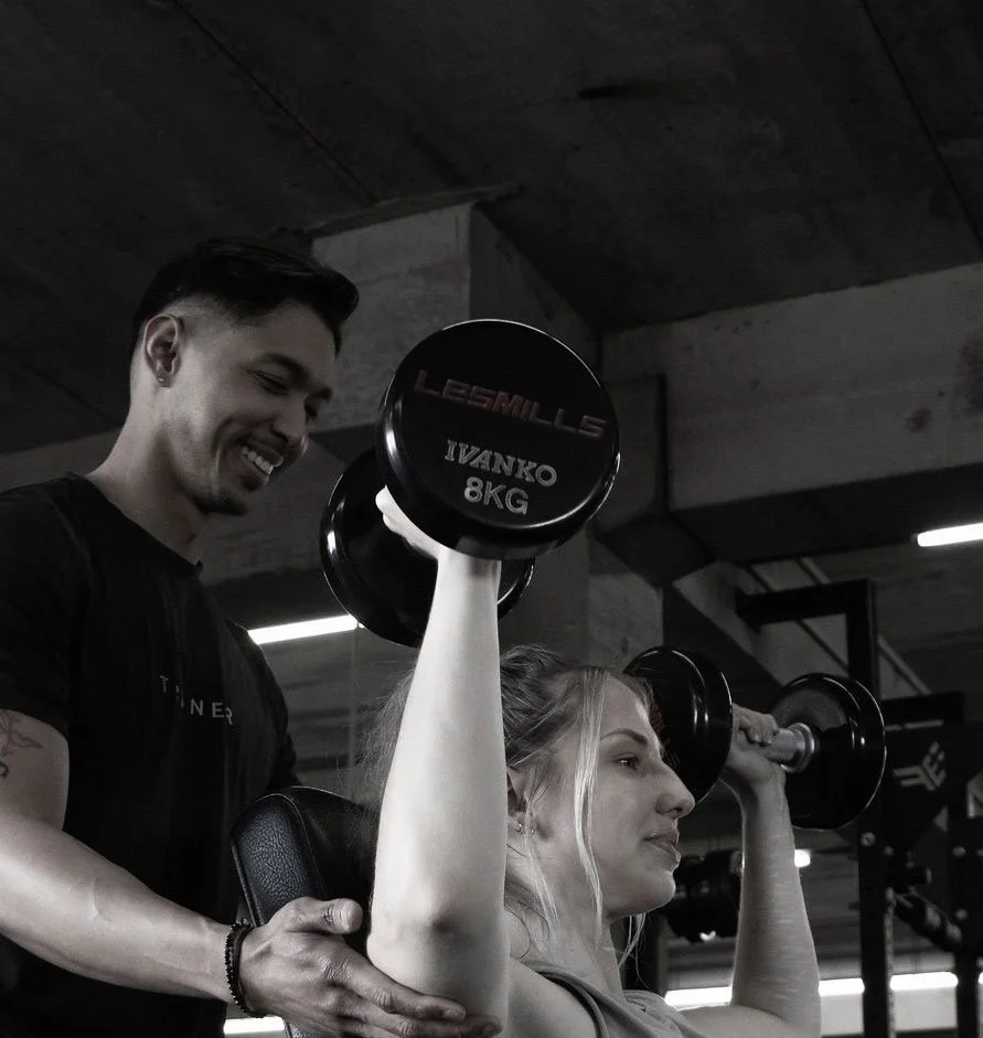 Woman lifting dumbbell while trainer assists at gym