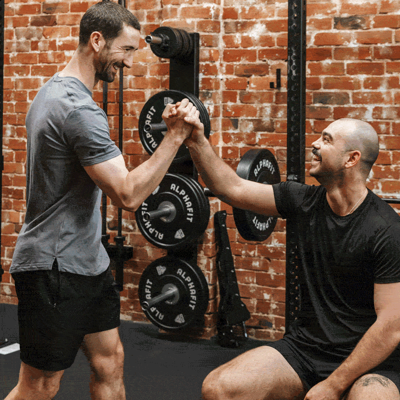 Two men working out at the gym with brick walls and weightlifting equipment.