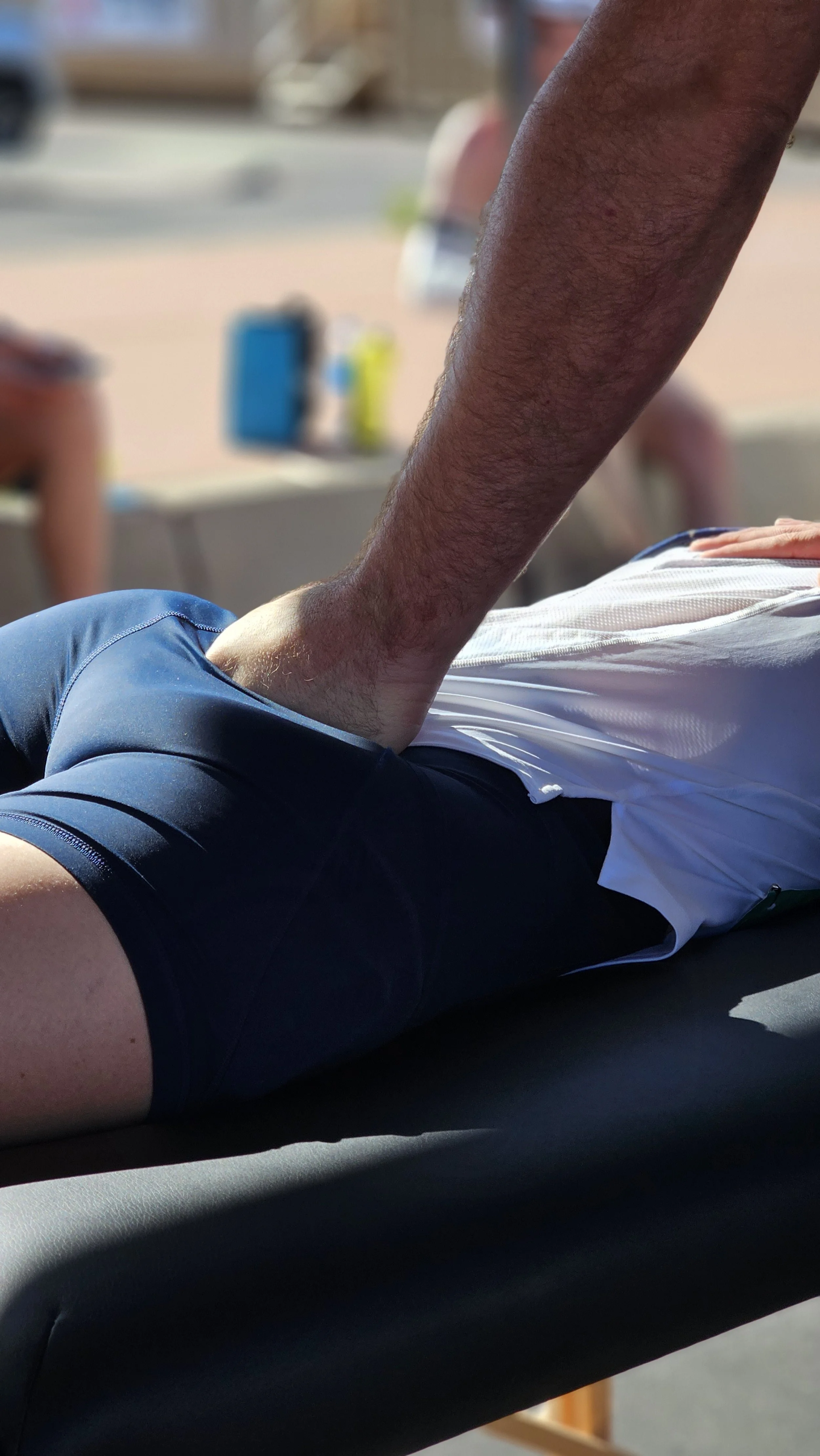 A person lying face down on a massage or therapy table, receiving a treatment or massage outdoors on a sunny day.