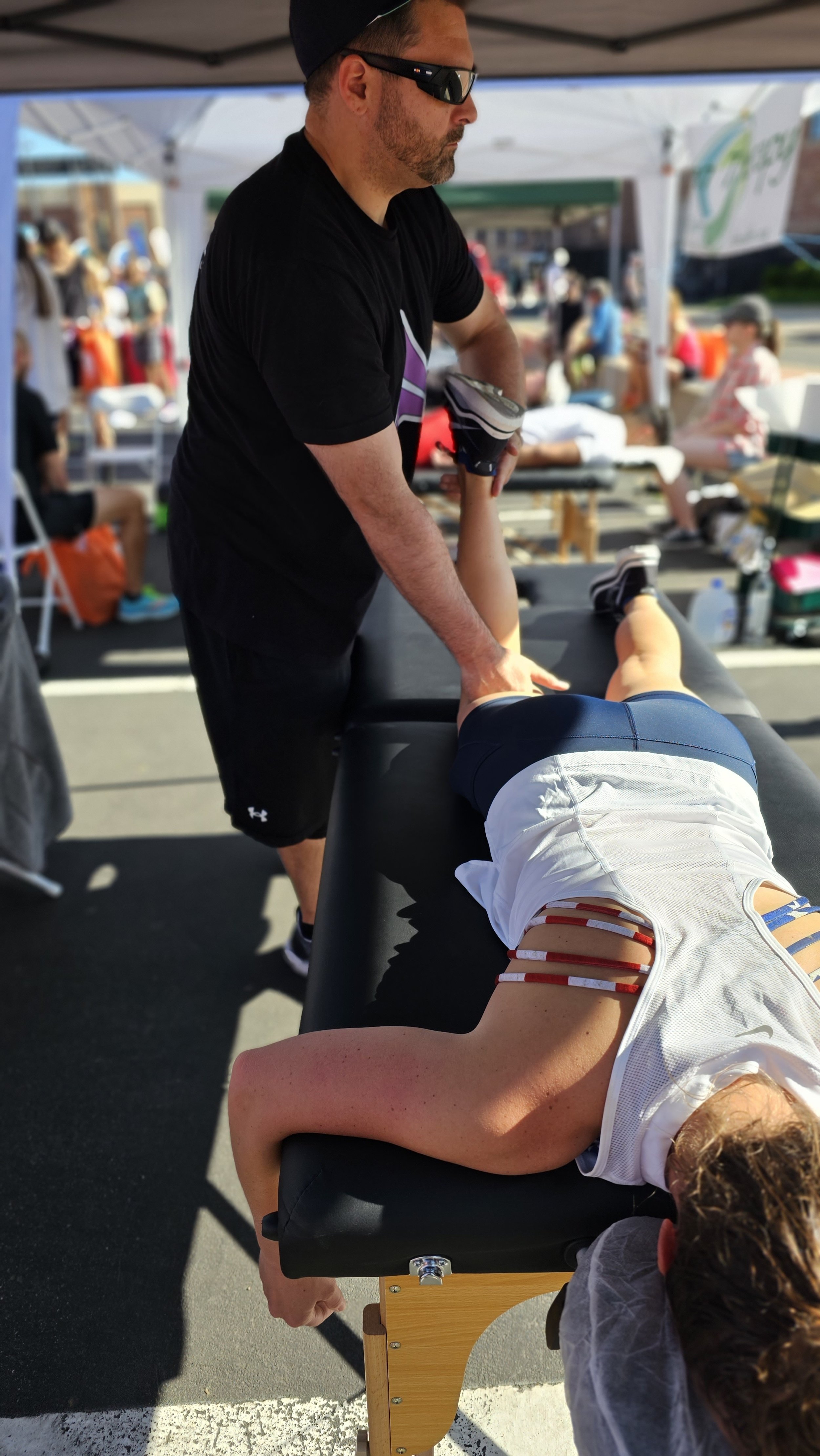 Matt Barcello providing sports massage on a runner’s leg at an outdoor Boulder event called BolderBoulder – Alleviate Sports Massage