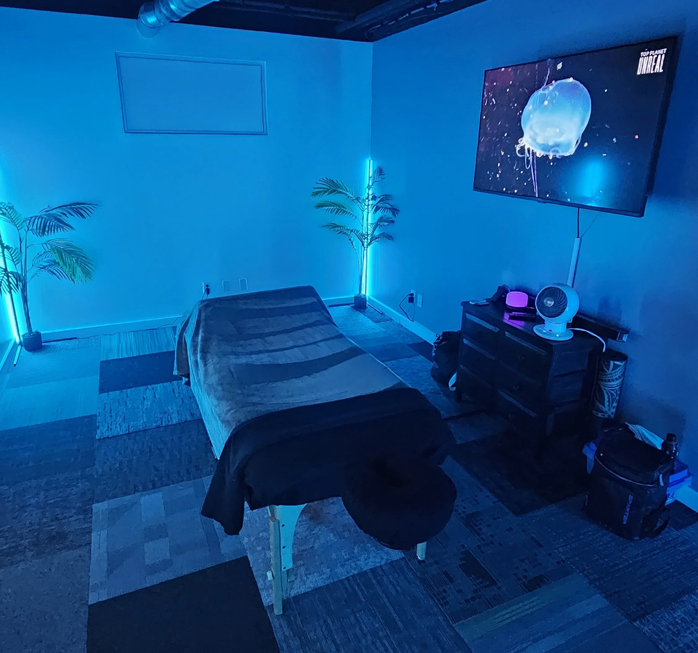 A massage room illuminated with blue LED lighting, containing a massage table at Alleviate Sports Massage