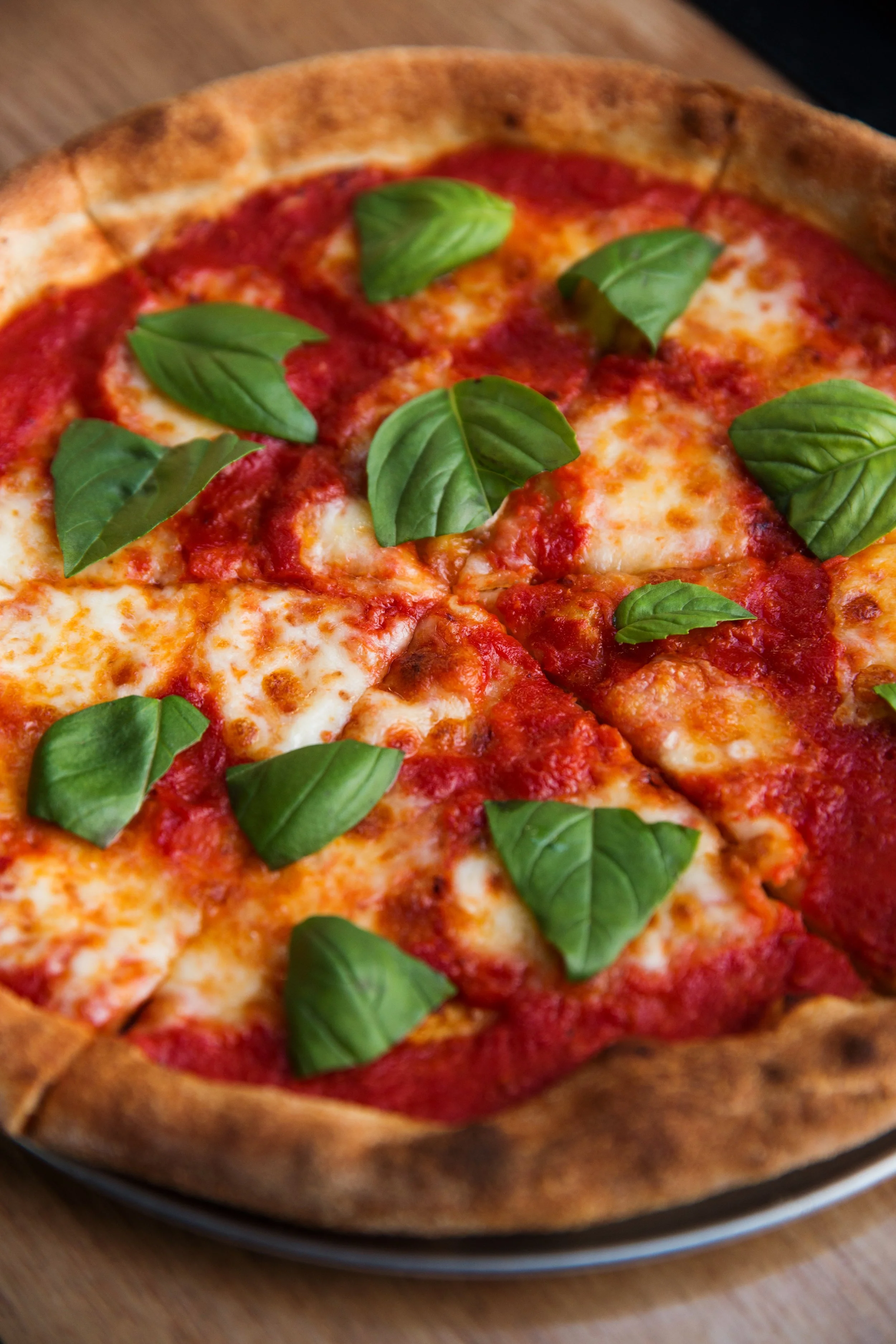 Close-up of a Margherita pizza with melted cheese, tomato sauce, basil leaves, and a golden-brown crust.
