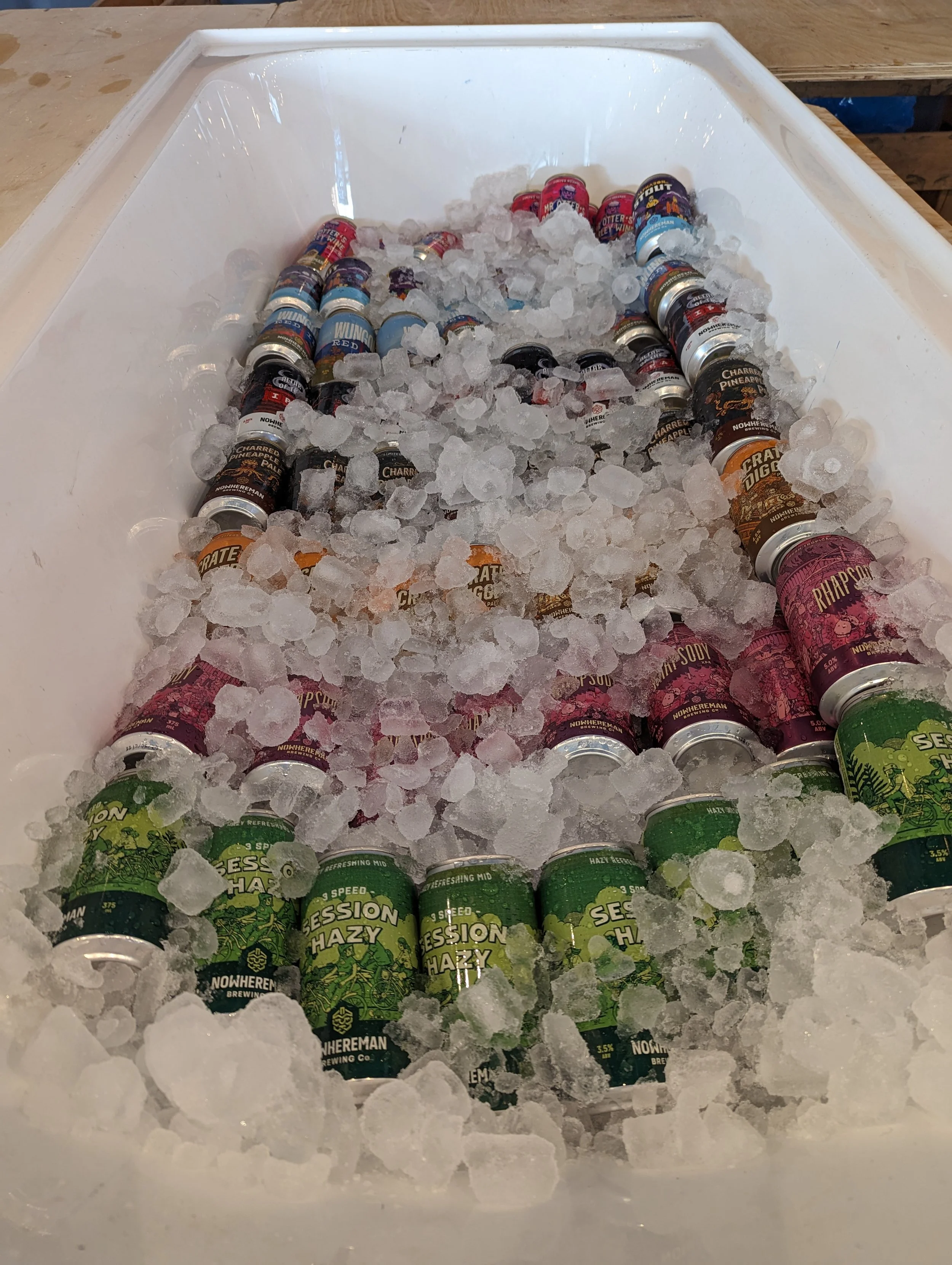 A white cooler filled with ice and various cans of different craft beers.