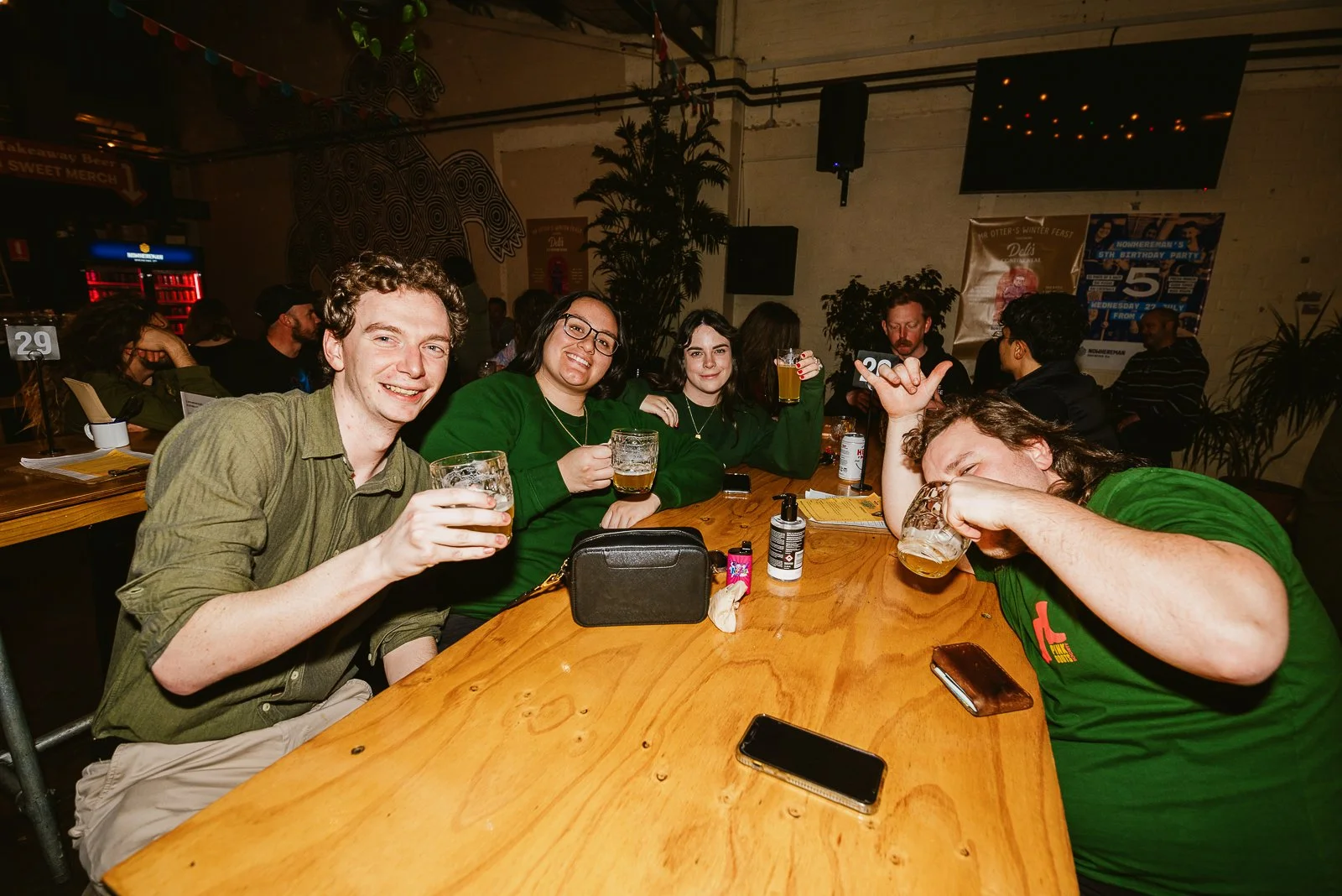 Group of friends enjoying drinks at a bar or restaurant, sitting around a wooden table, smiling and celebrating.