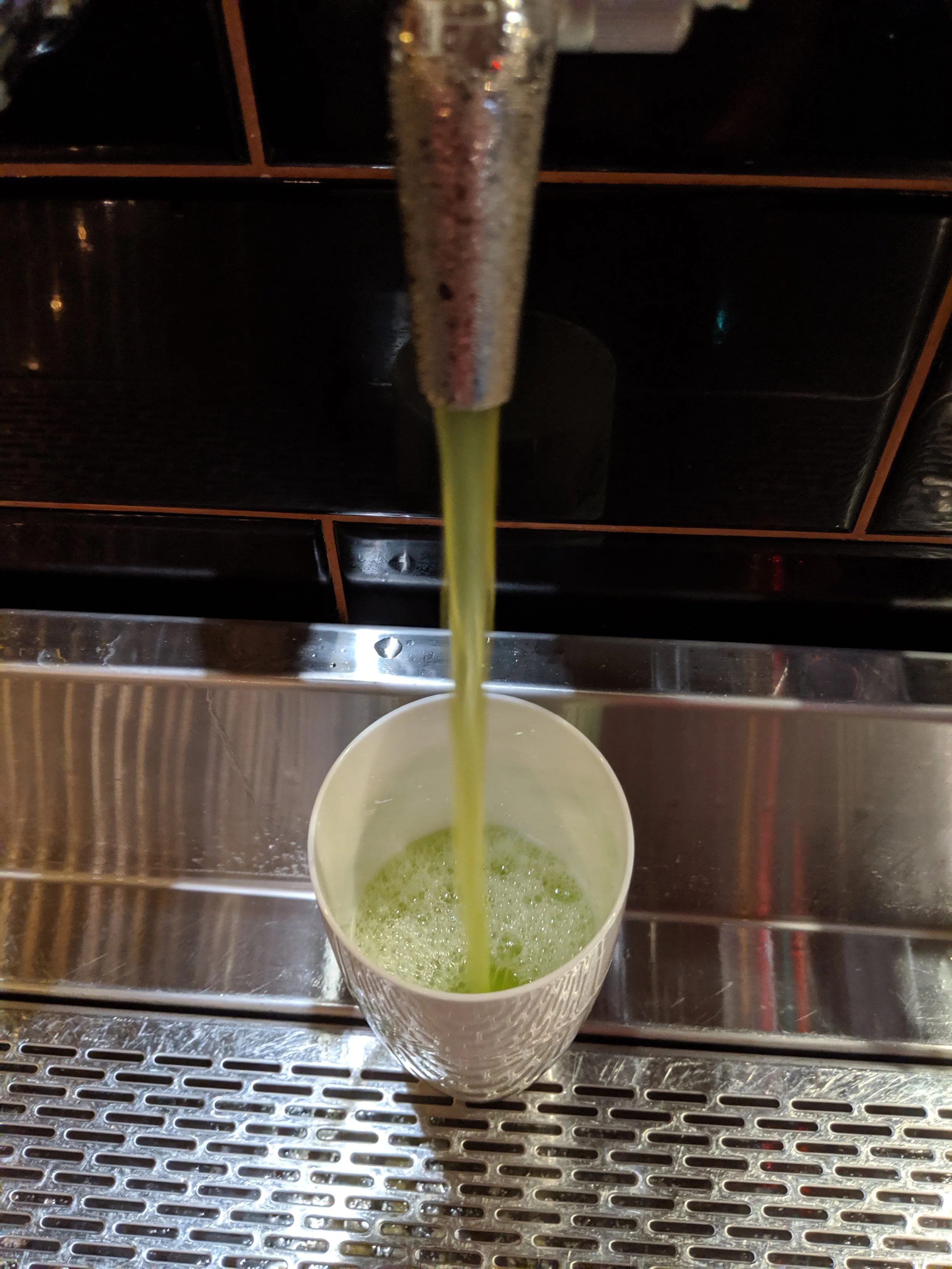 Green juice being poured from a dispenser into a white cup.