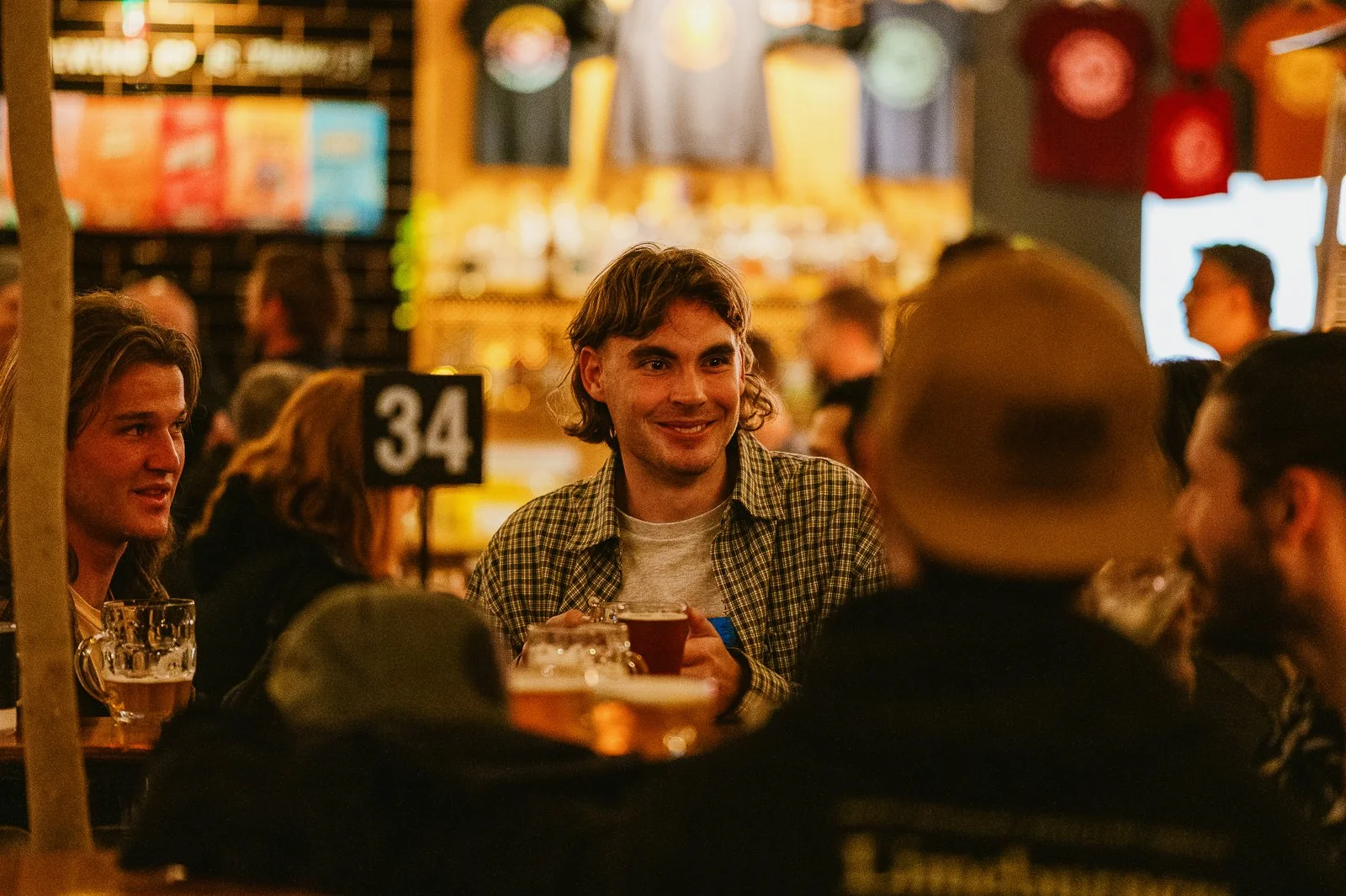People sitting at a bar, drinking beer and socializing in a lively pub with warm lighting.