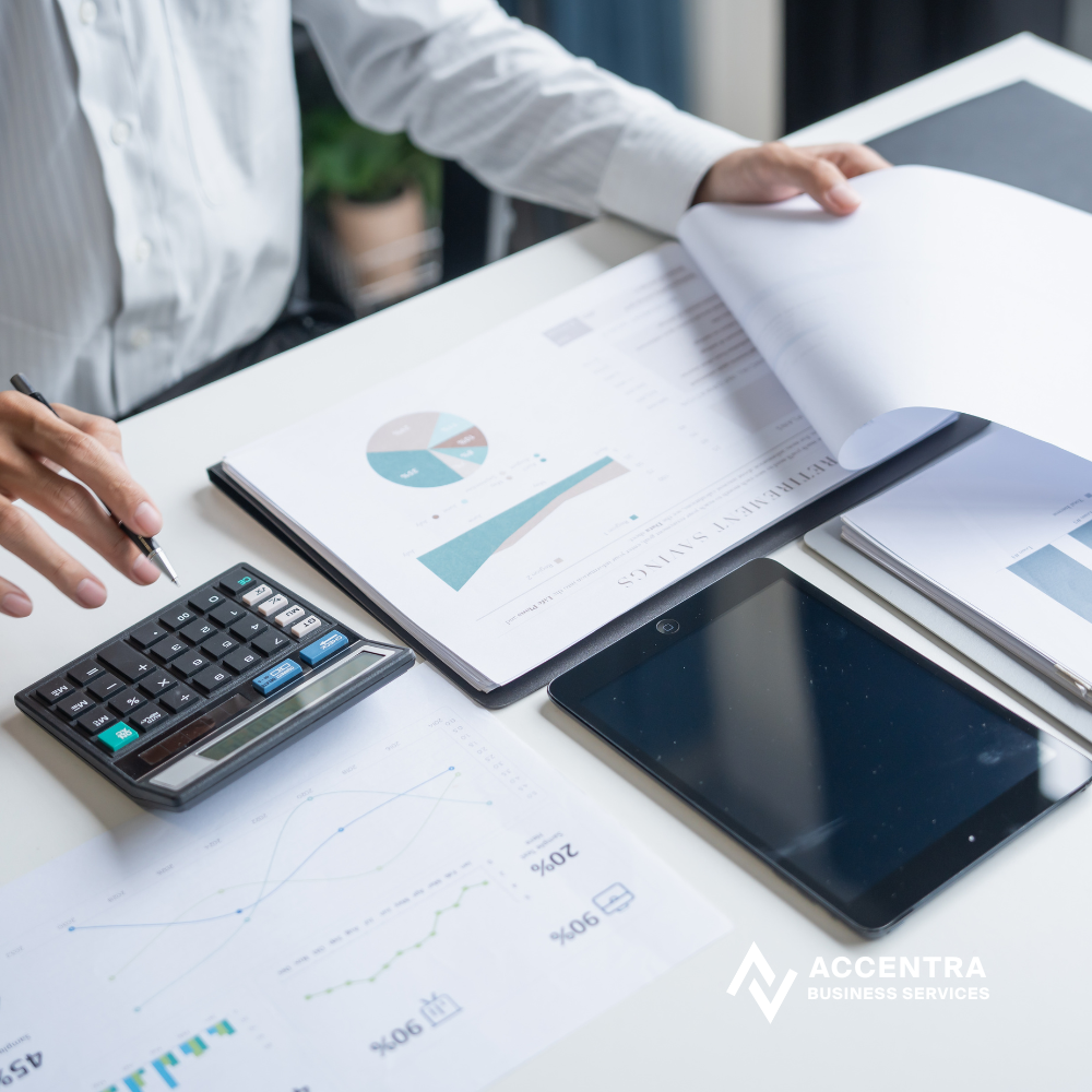 Business person working at desk with financial reports, calculator, tablet, and documents with charts and graphs.