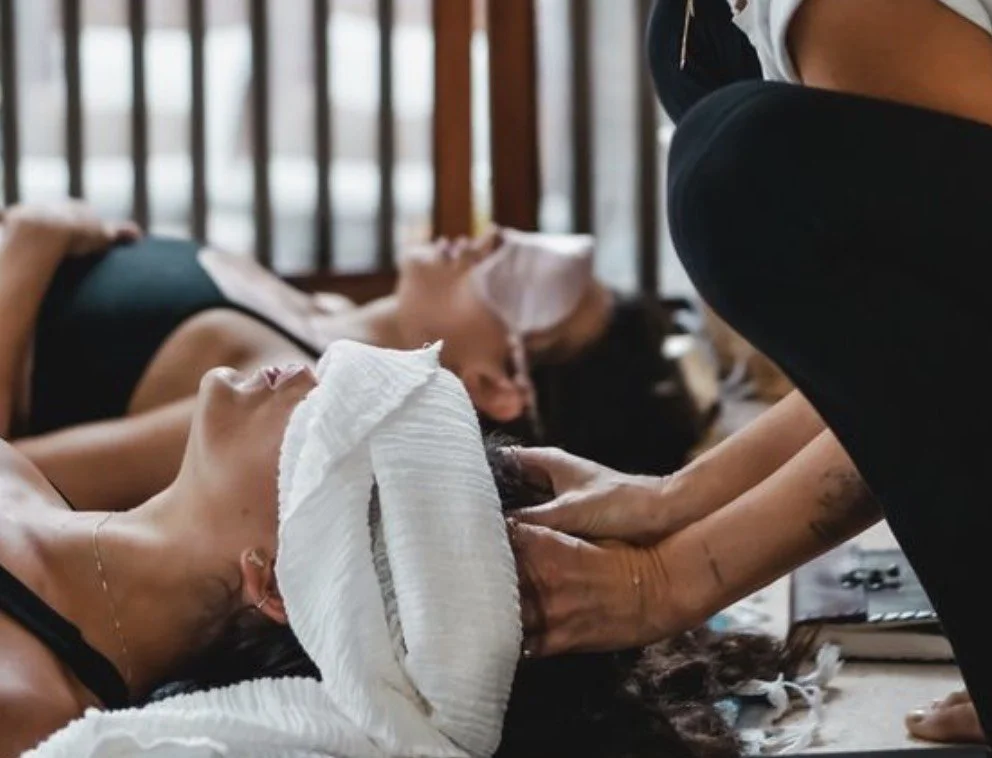 Three women are receiving head or scalp massage while lying down on mats with towels on their heads.