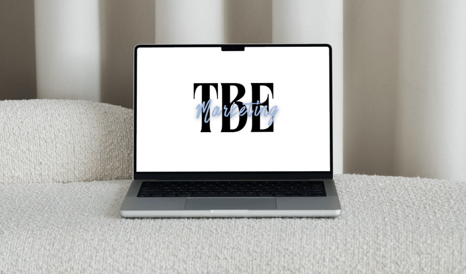 Laptop on a beige textured surface displaying a graphic with the words 'Trade Marketing' in black and blue font.