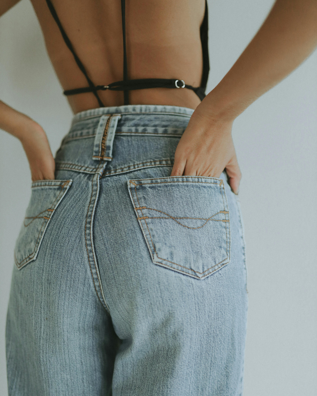 Back view of a person wearing light blue high-waisted jeans and a black strappy top.